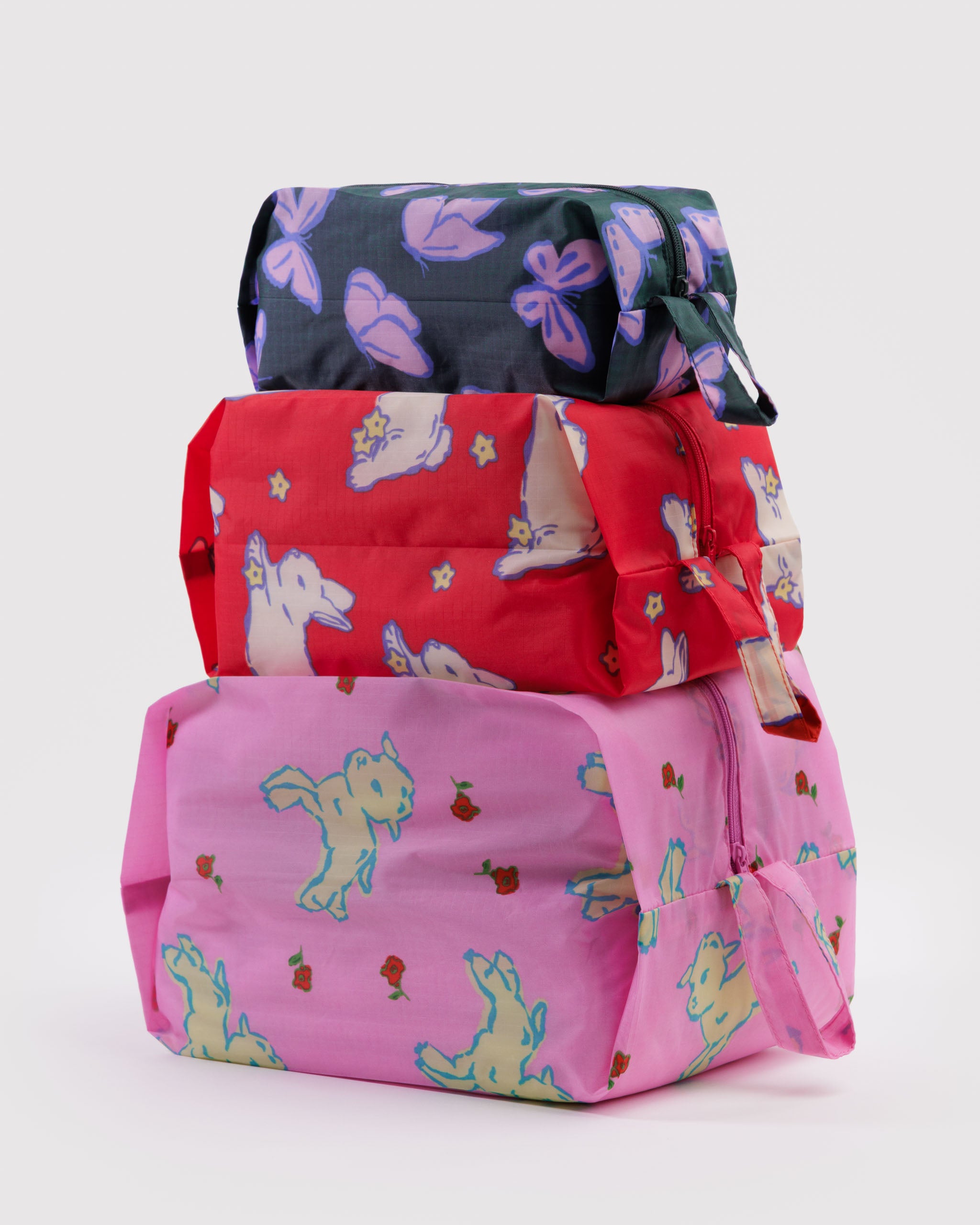 Stack of 3 different sized colourful bags with spring animal patterns expanded with items inside, with zip closure and hanging loop.