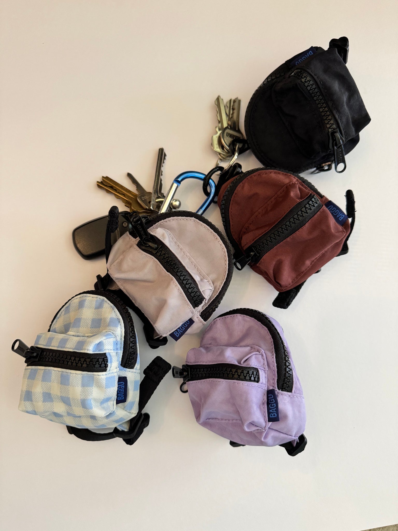 Five ultra-mini backpack style bag charms in various colours with keys attached.