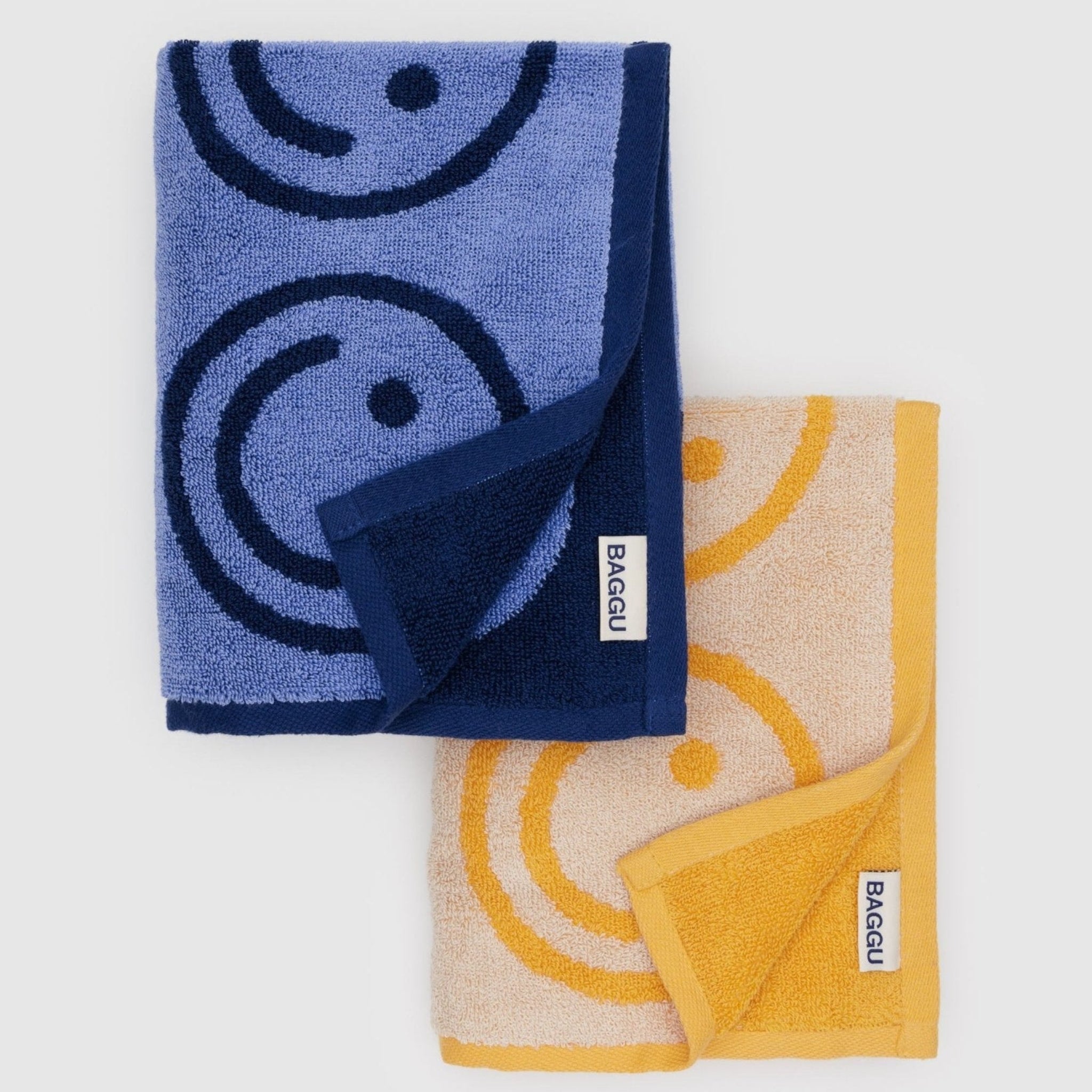 Folded set of a blue and a yellow hand towels with smiley face print with BAGGU label.