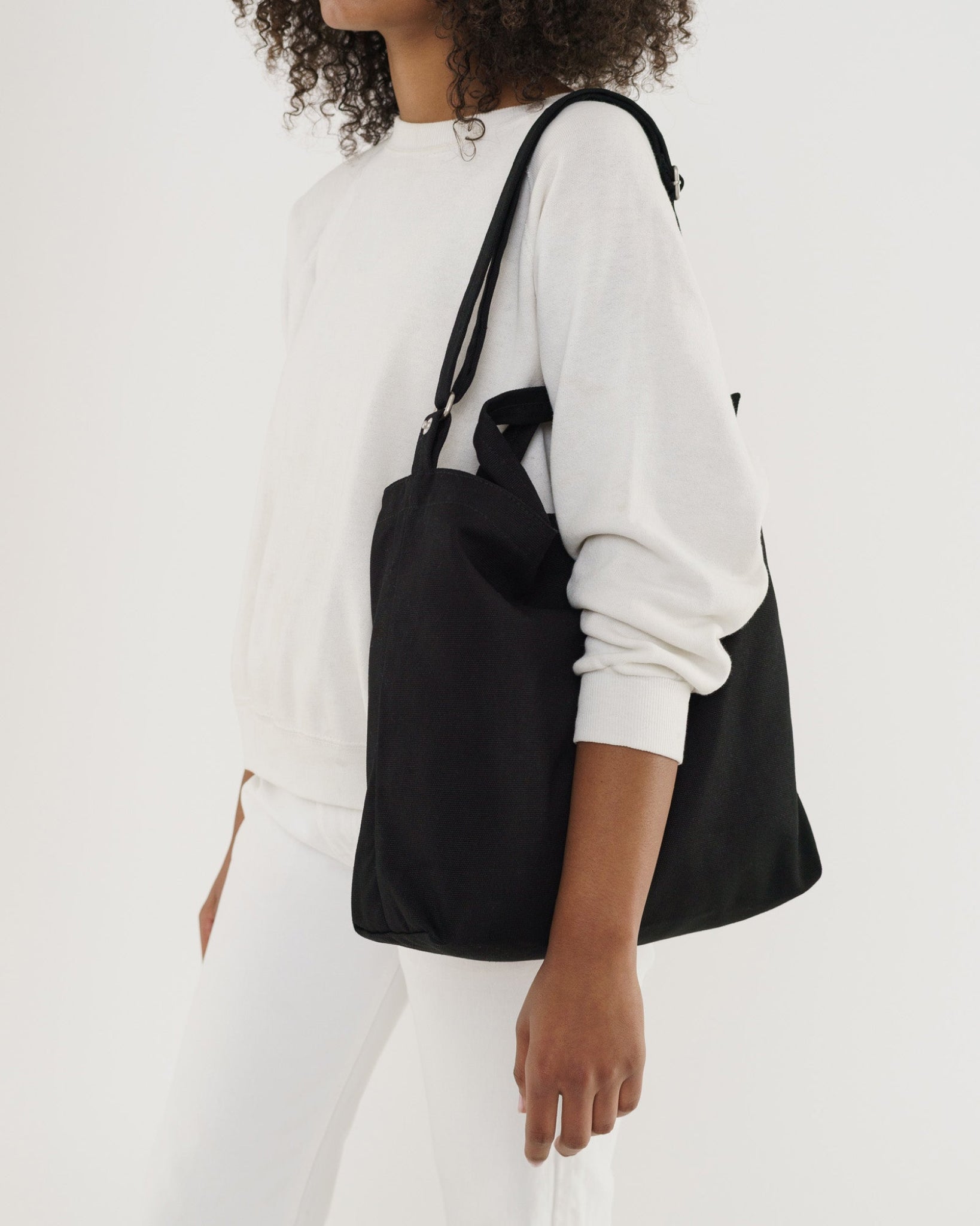 Person carrying a black tote bag over one shoulder with the adjustable strap.