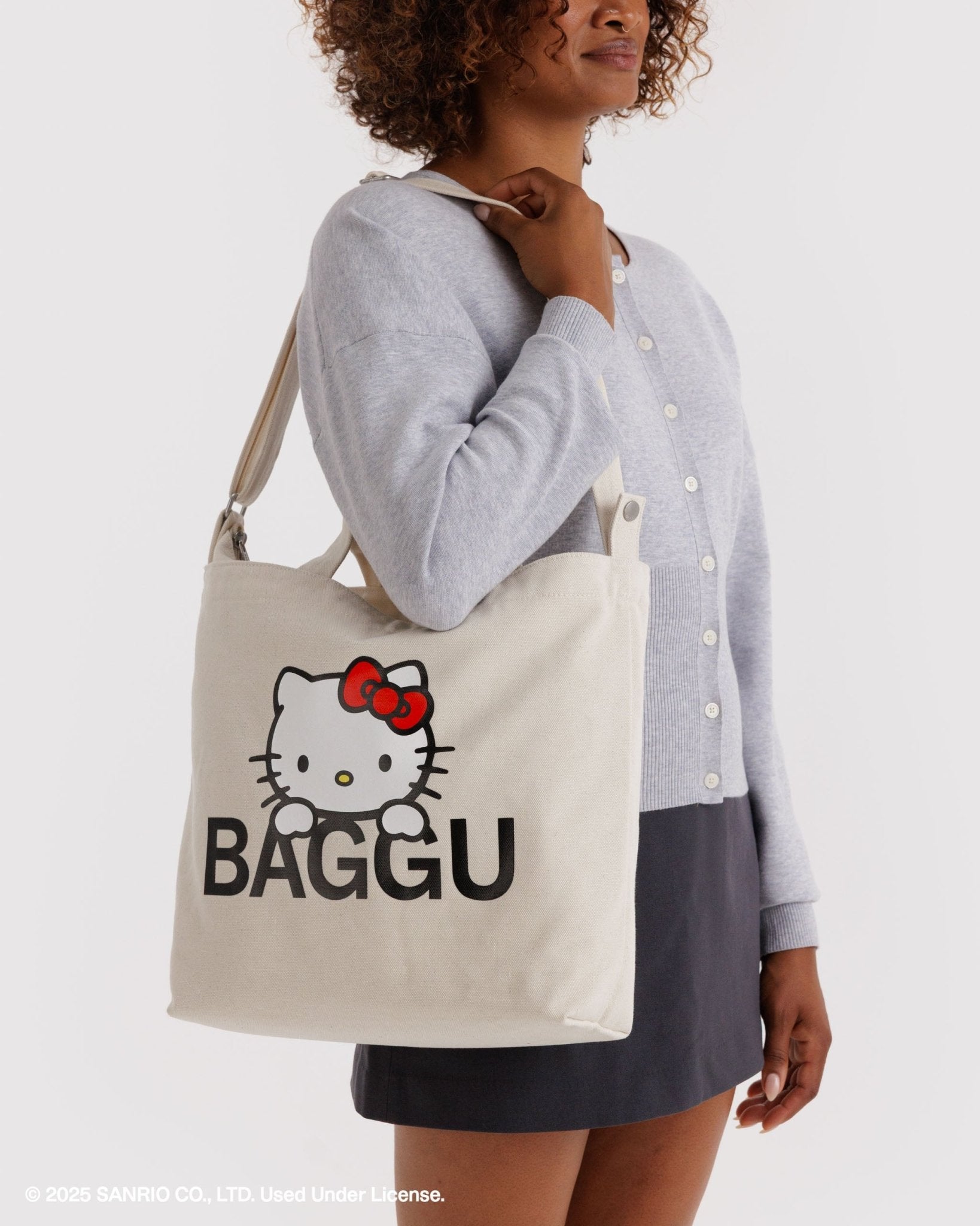 Person holding a beige tote bag with a Hello Kitty logo and 'BAGGU' text on a white background