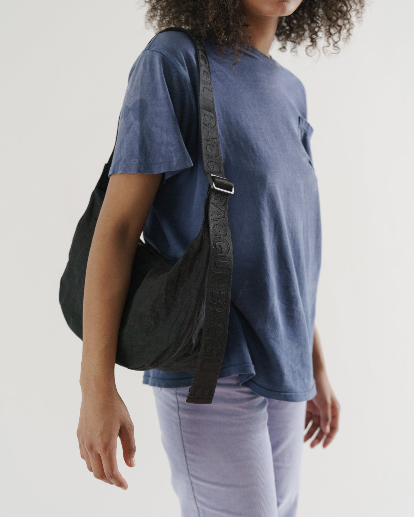 Person wearing a blue shirt and light-coloured pants carrying a black bag with adjustable strap over one shoulder.