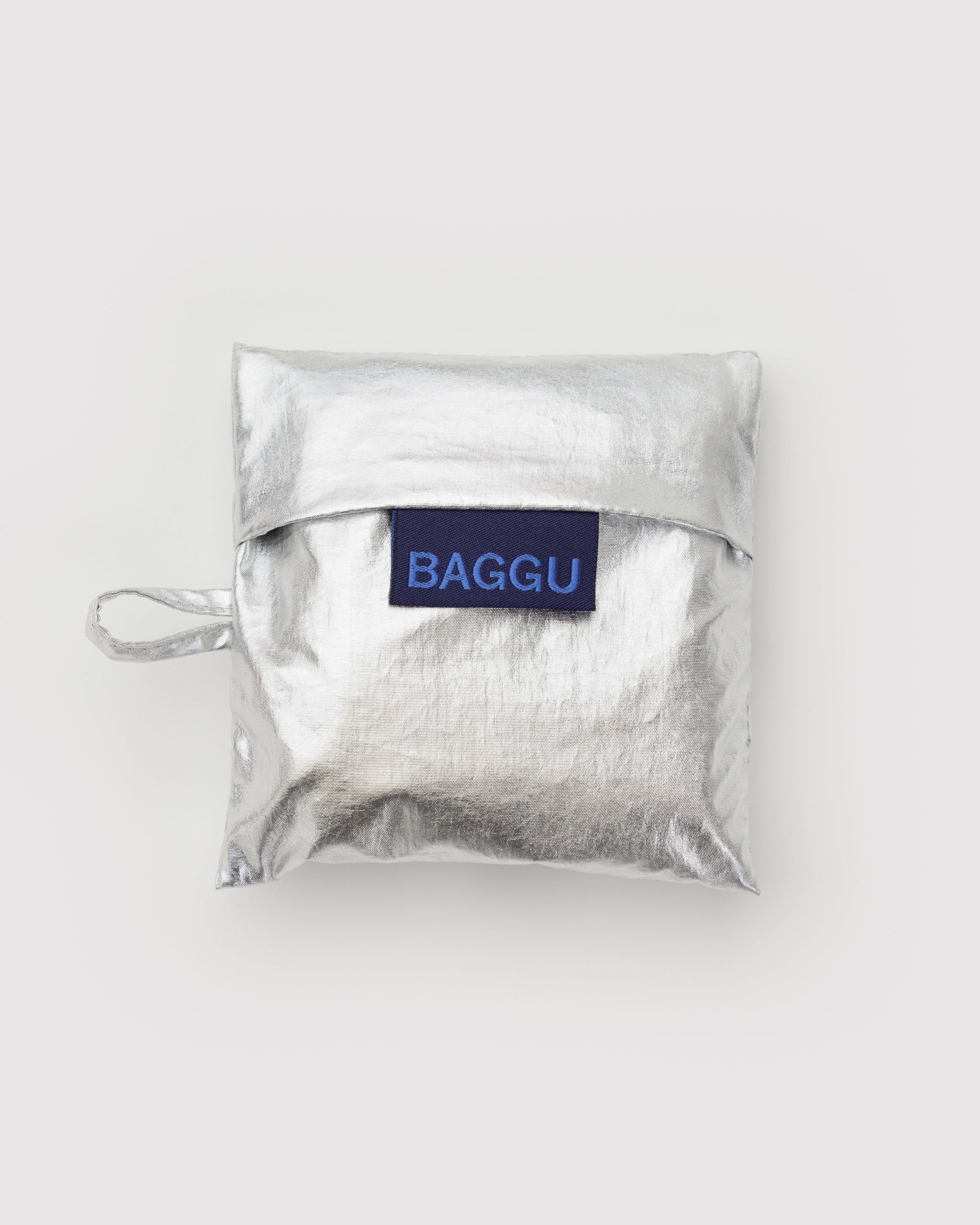 Silver foldable pouch for reusable bag with 'BAGGU' label and hanging loop.