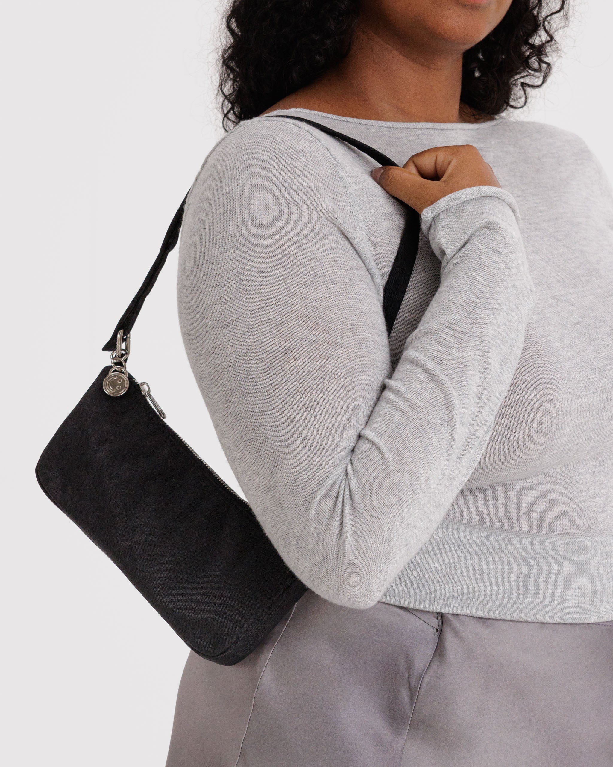 Person wearing a small black nylon shoulder bag with silver metal charm and top zipper over one shoulder.
