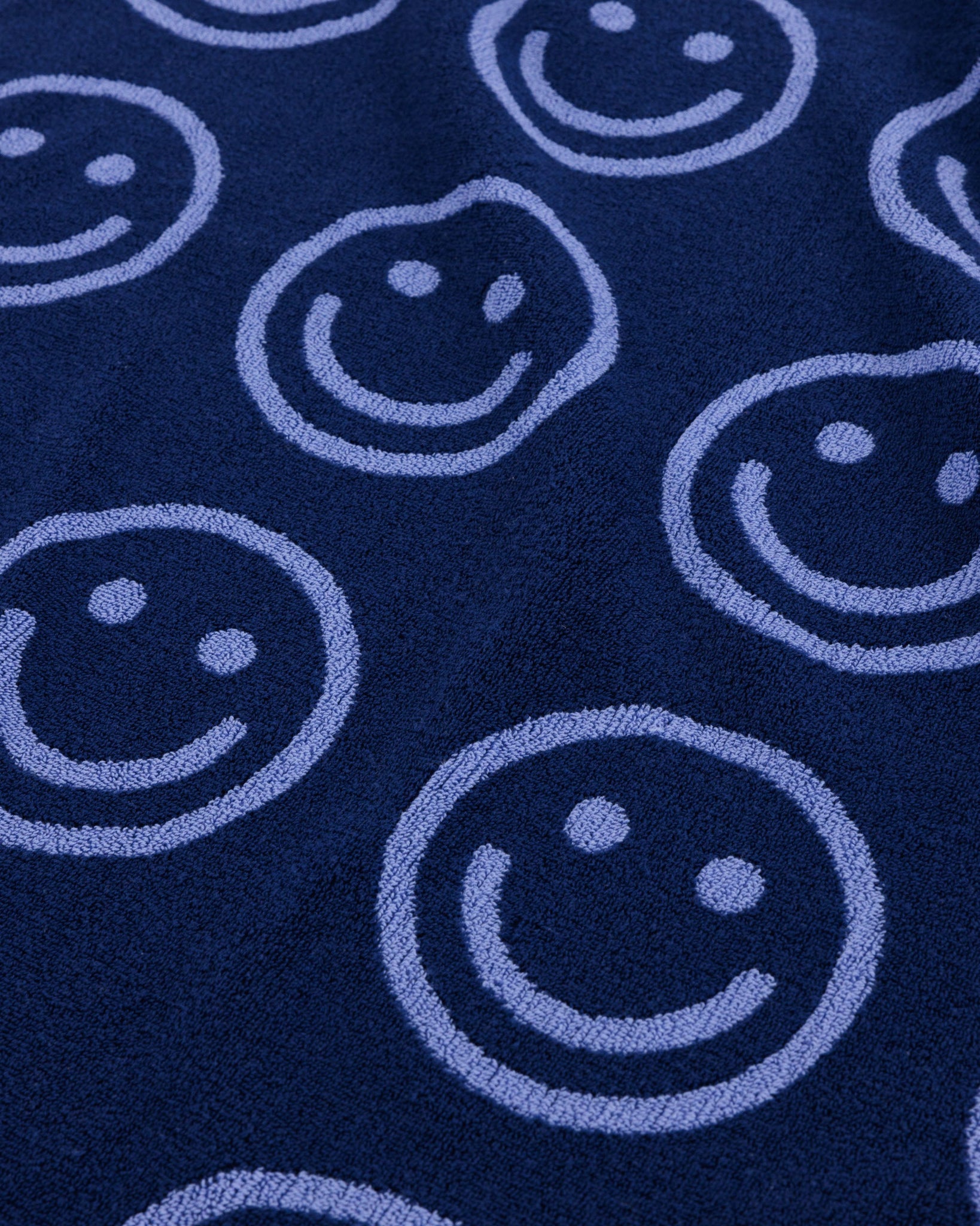 Close up of navy blue towel fabric with light blue smiley face patterns.