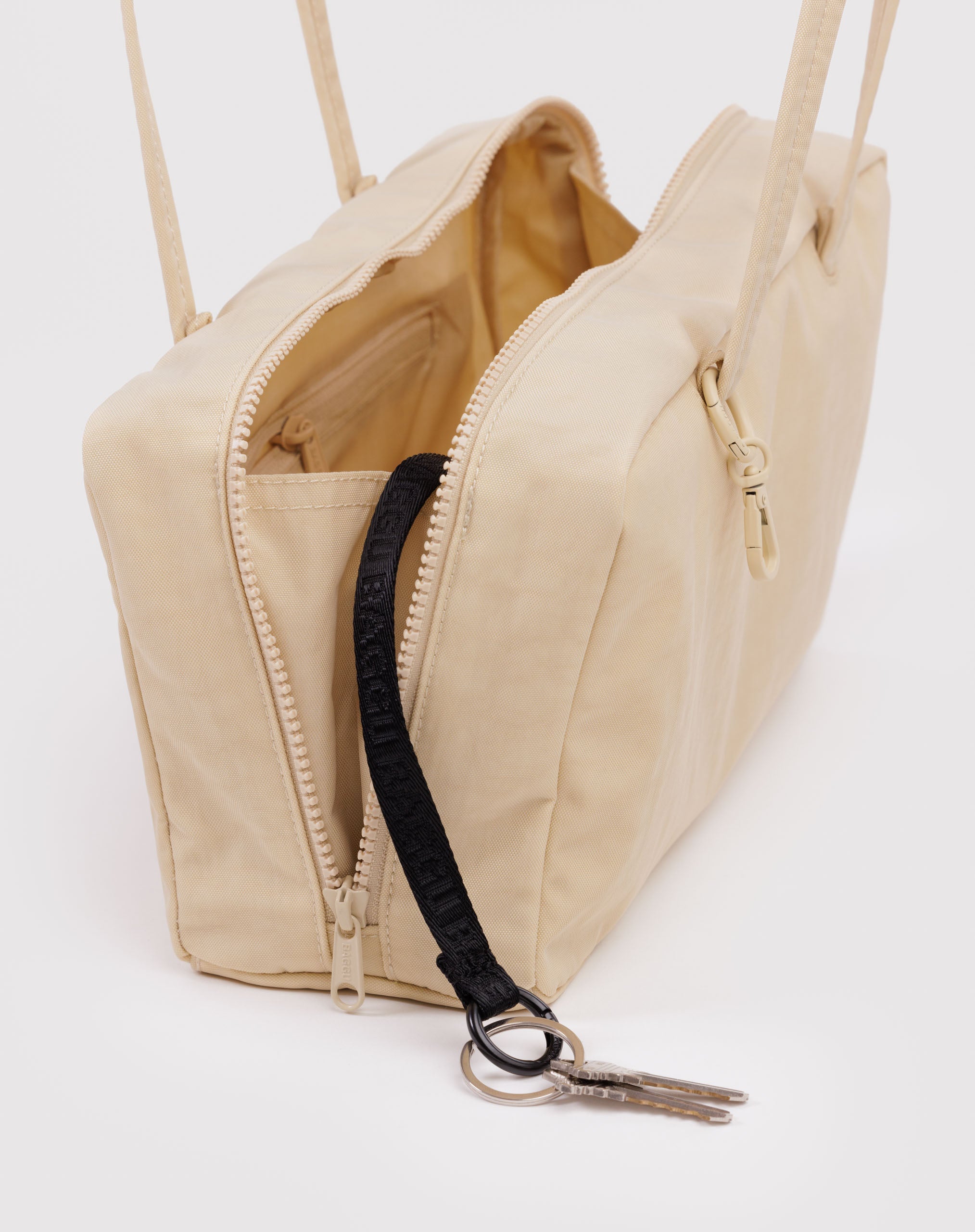 Light yellow handbag with top zips open and a black keychain with keys.