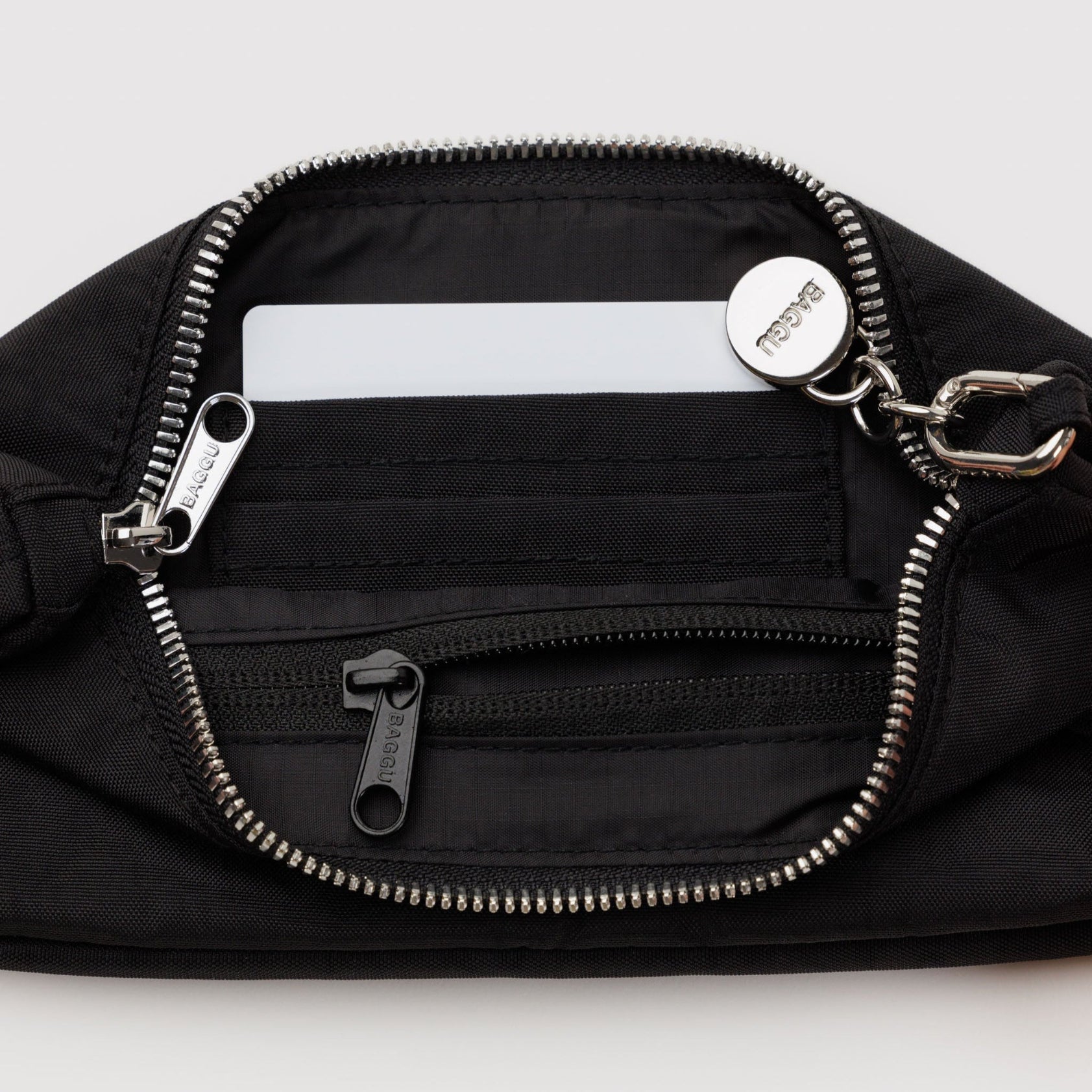 Black bag with top open zipper and internal zip pocket and card slots with adjustable metal clasp for shoulder strap and charm.