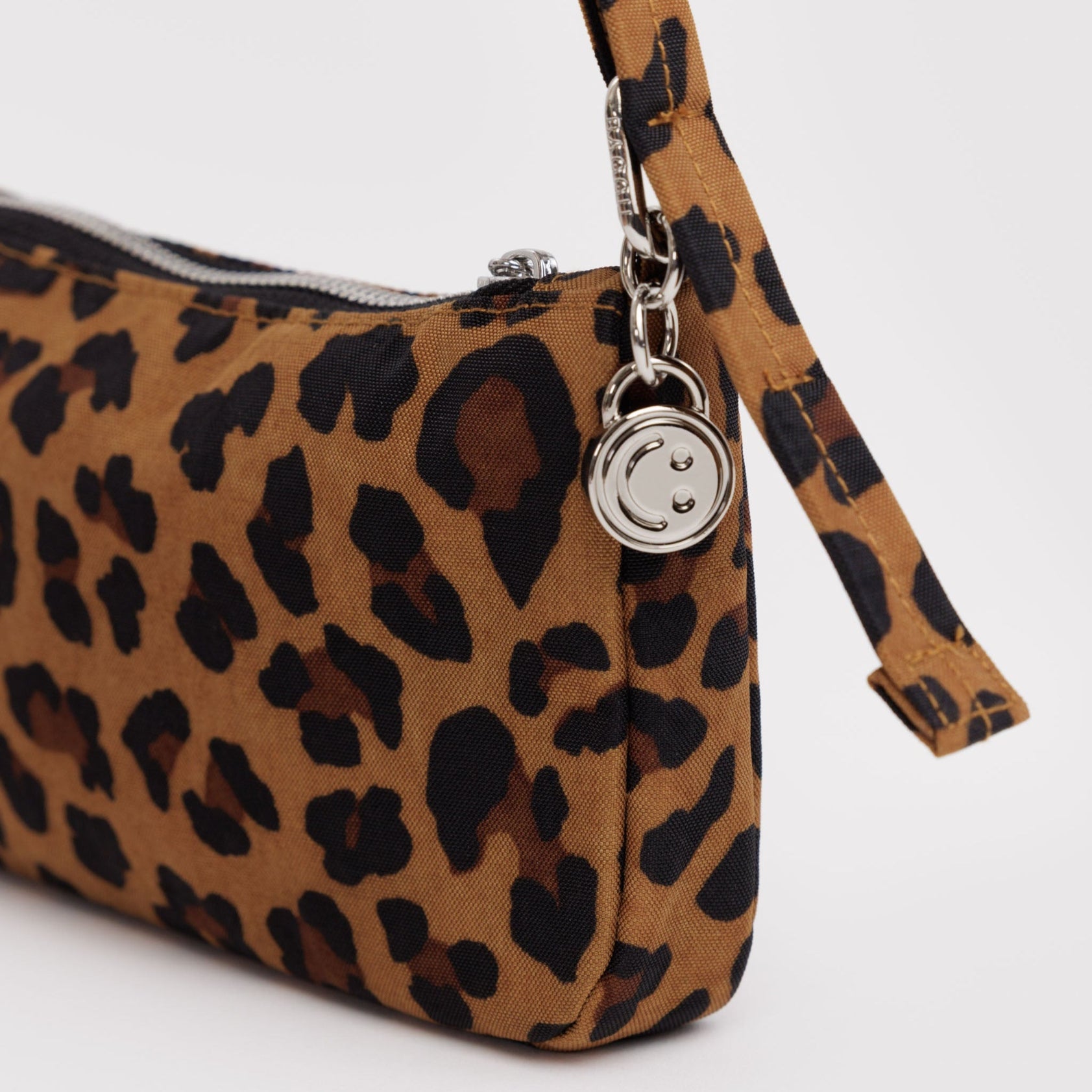 Small nylon Leopard print handbag with a adjustable strap and silver hardware clasp, smiley face charm and zip.