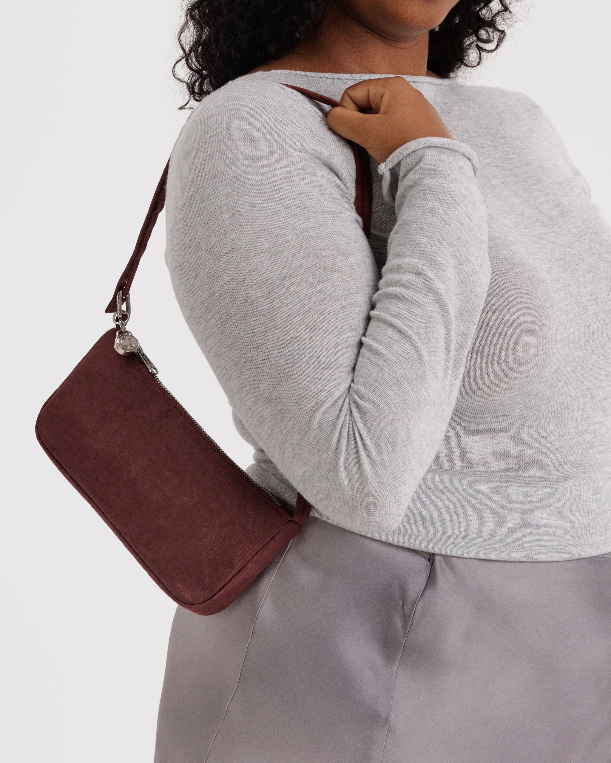 Person holding a small burgundy nylon bag with silver metal charm and top zipper over shoulder.