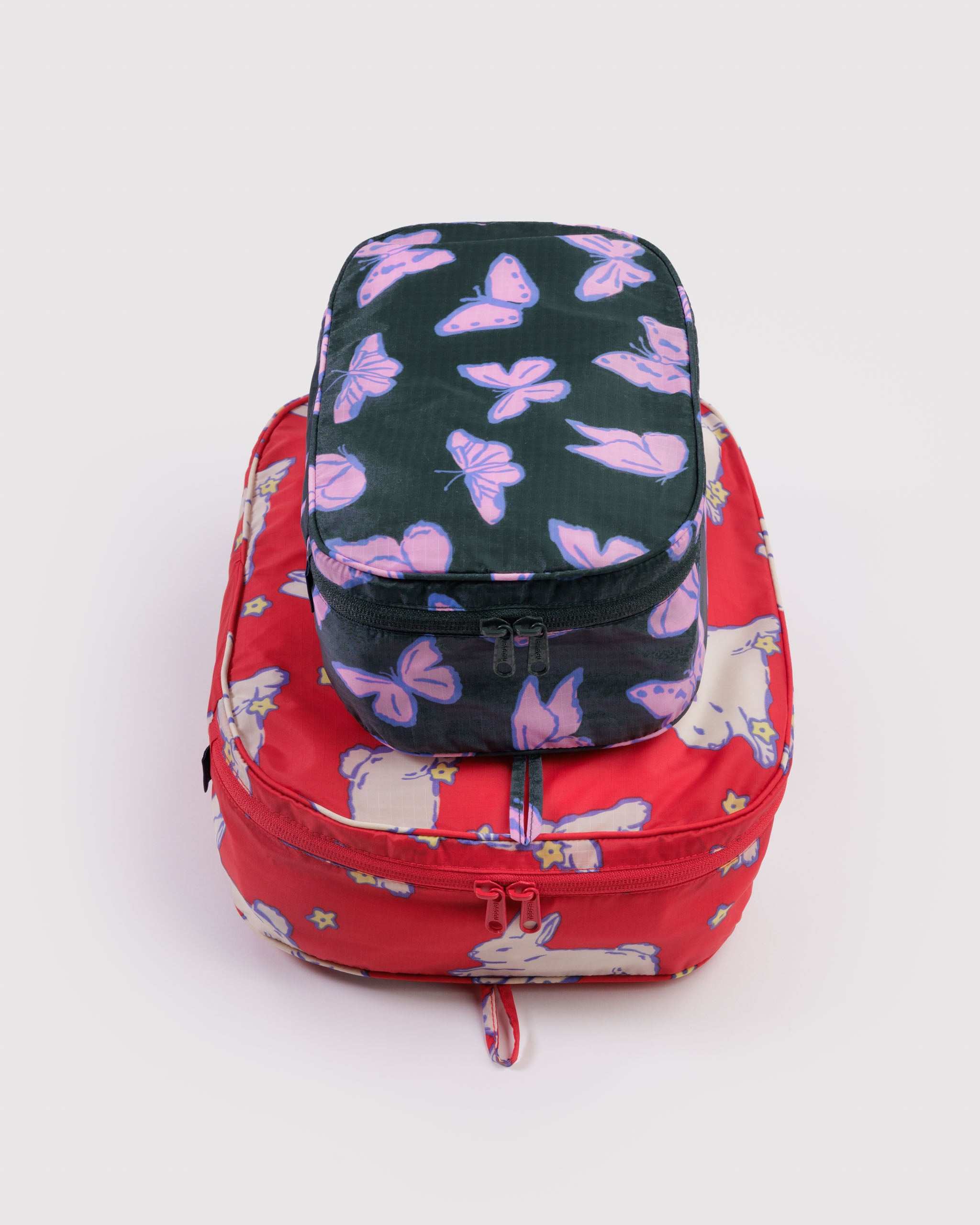 Red with white lambs and teal with butterflies prints on travel packing cubes set in small and medium size with all around tonal zippers.