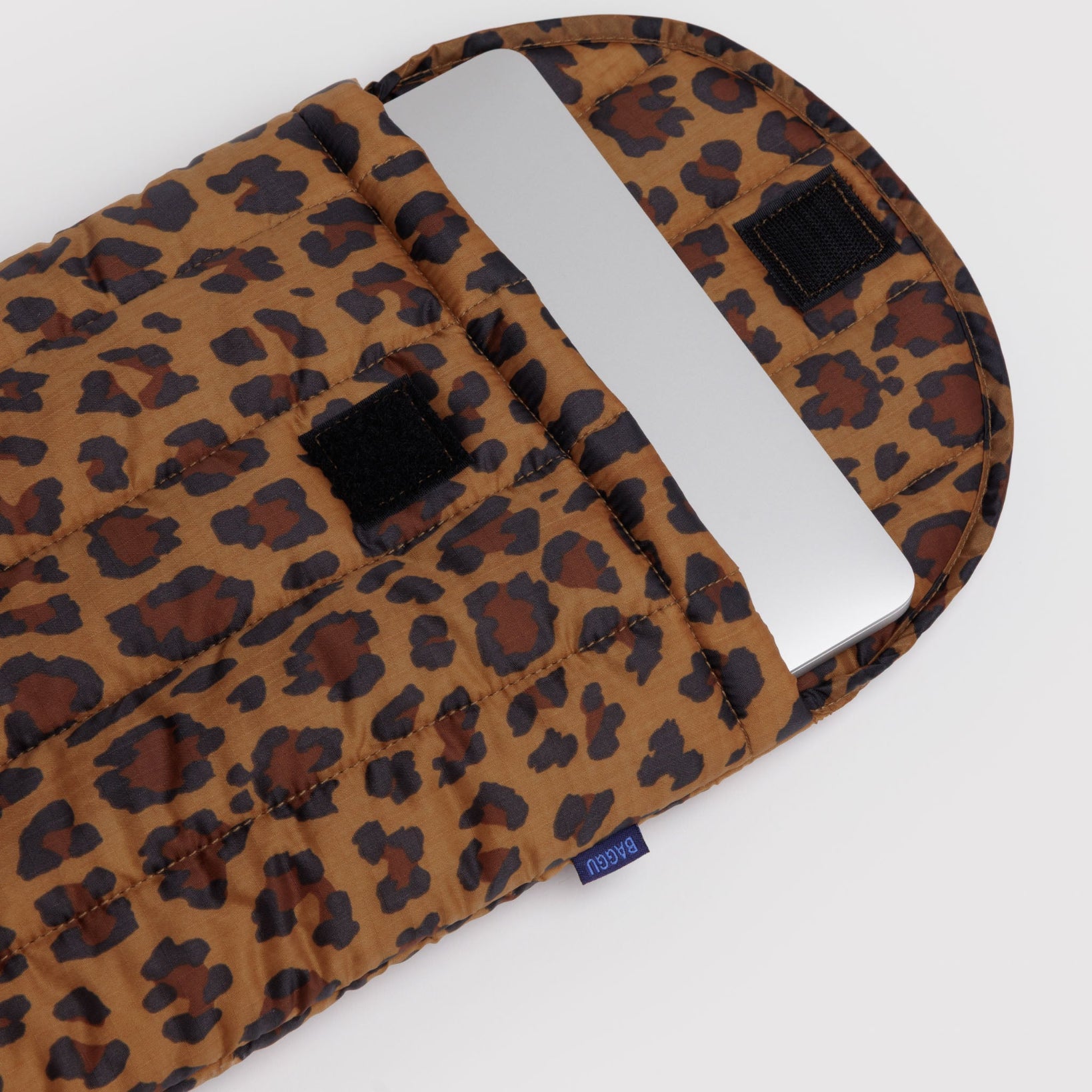 Leopard print quilted laptop sleeve with a silver laptop inside and velcro flap open and BAGGU label at side.
