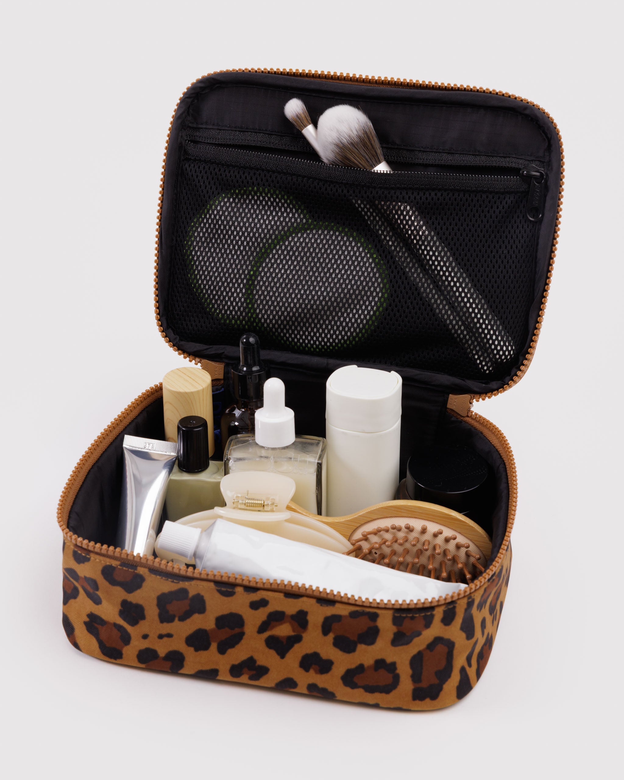 Leopard print cosmetic bag containing various toiletries with brushes in the mesh zip pouch on the inside of the lid.