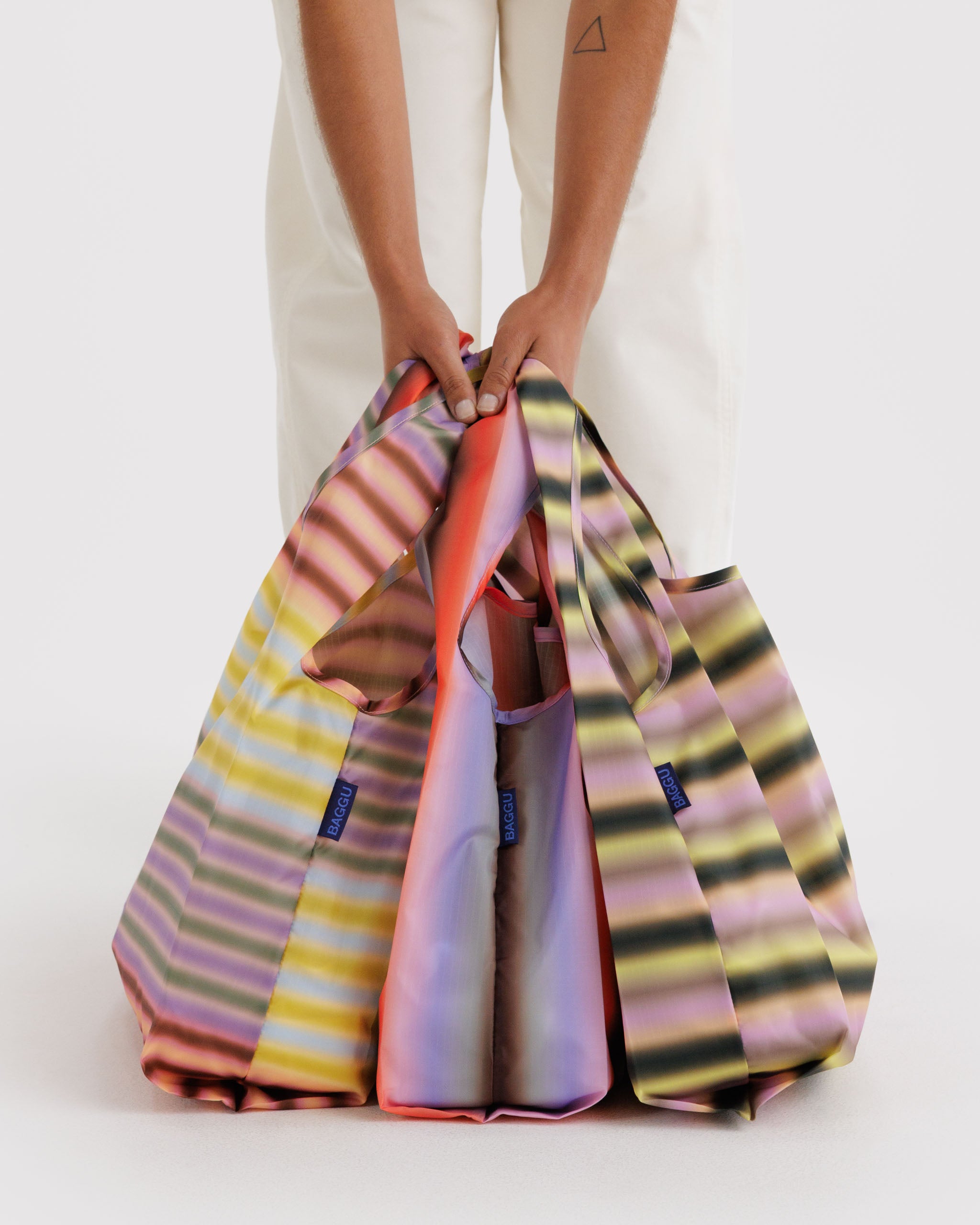 Three multicolored striped bags held by a person.