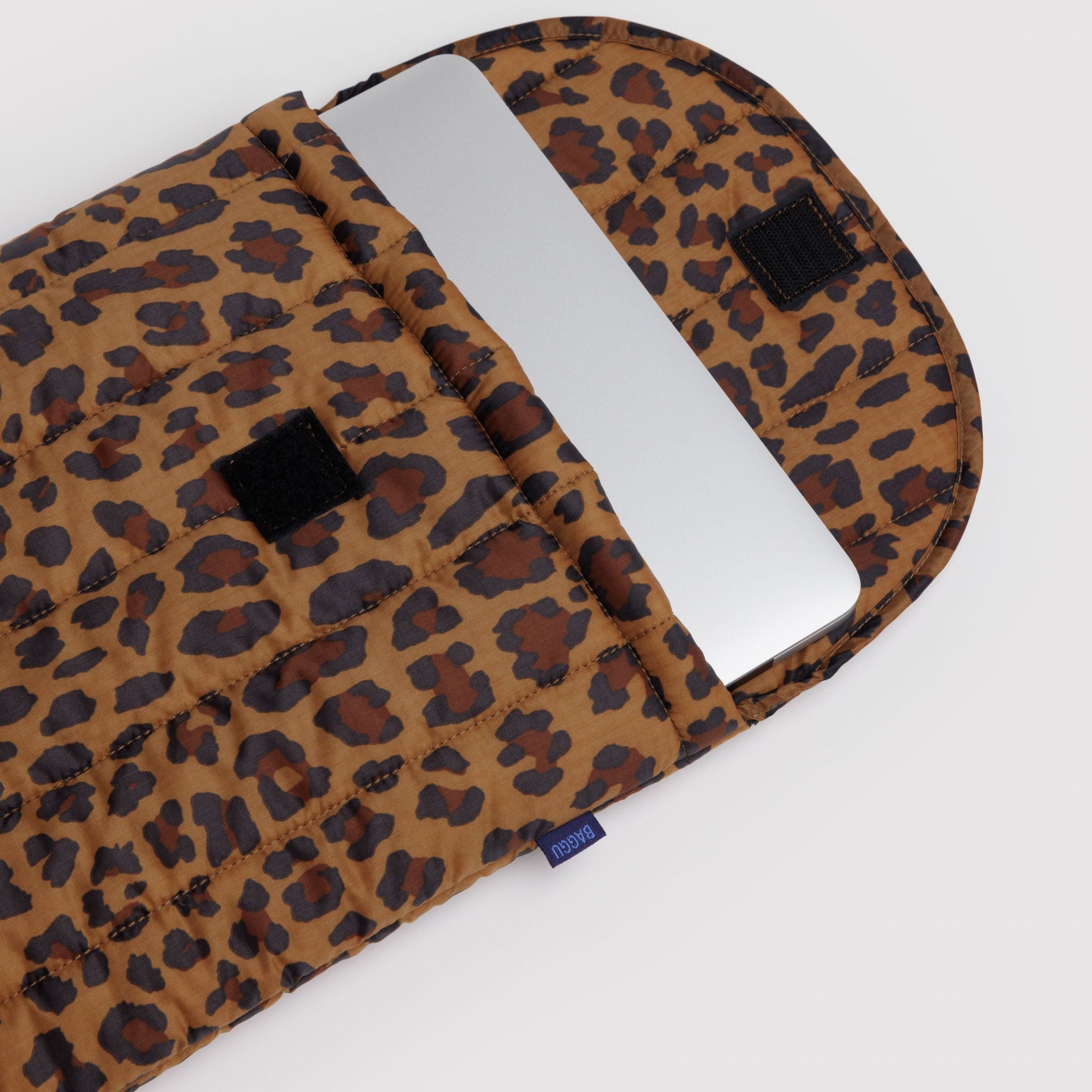 Quilted and puffy leopard print laptop sleeve with a silver laptop inside and velcro top opening.