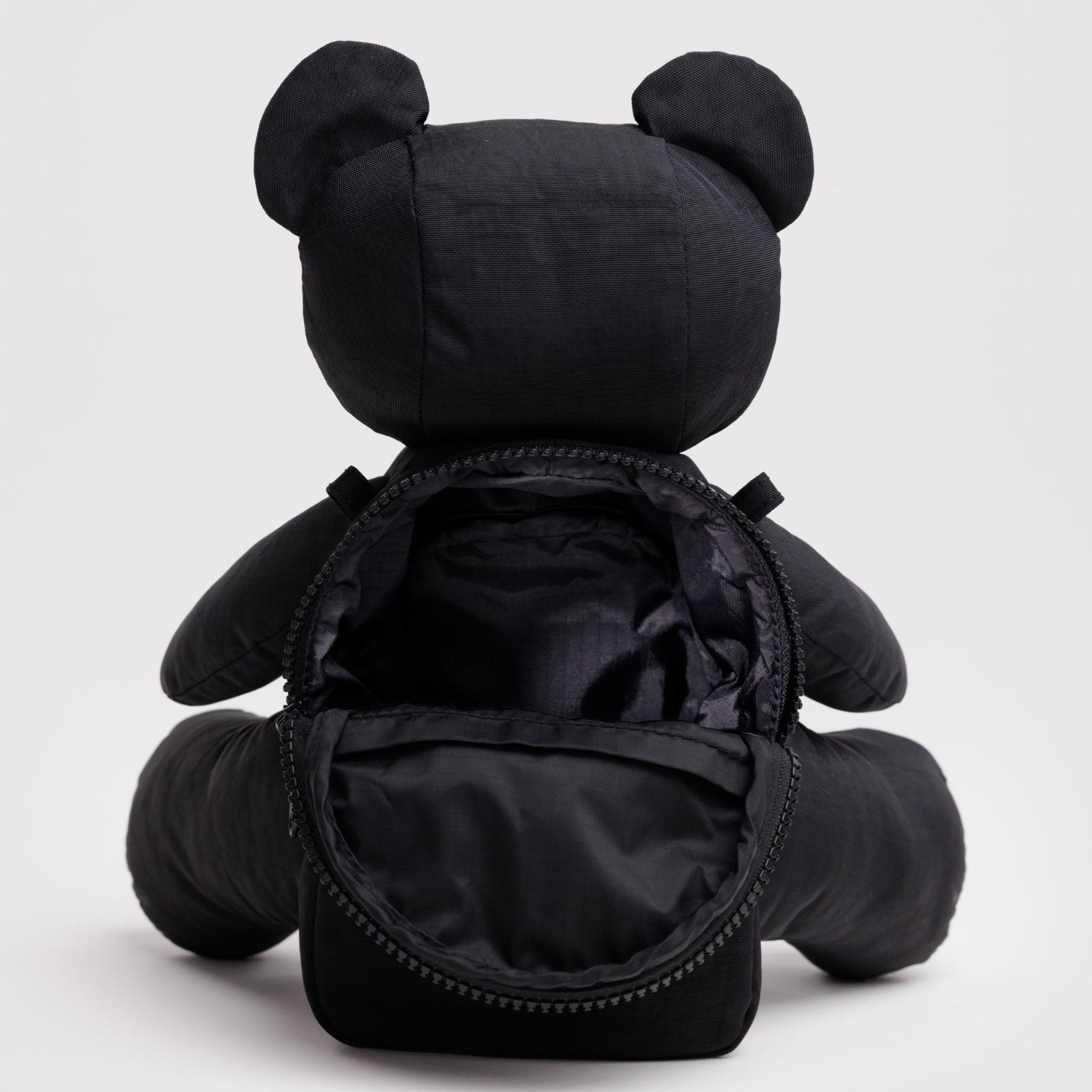 Black teddy bear bag with open zip pouch at back.
