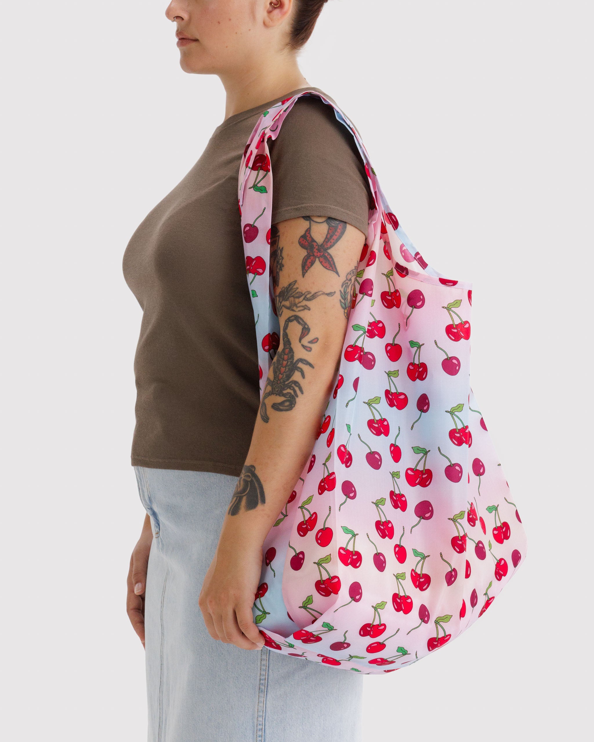 Woman carrying a pink reusable tote bag with cherry pattern on shoulder.