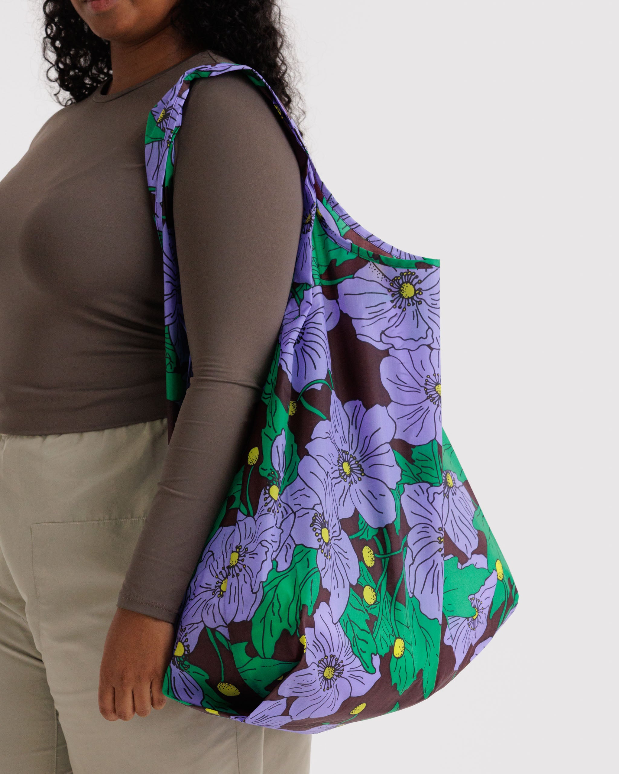 Person wearing a purple floral poppy reusable tote bag on shoulder.