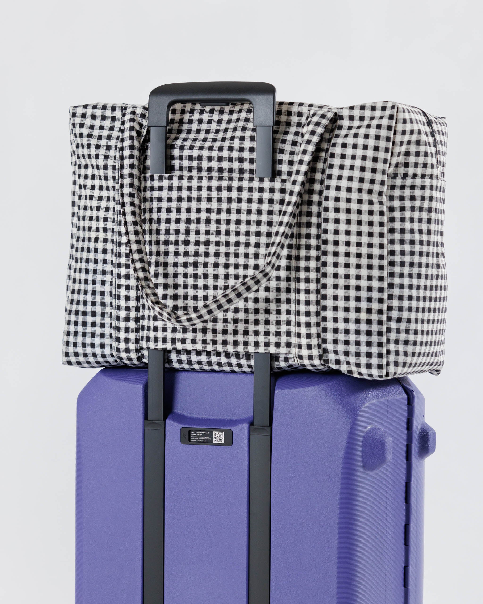 Baggu-cloud-carry-on-in-black-and-white-gingham-on-top-of-suitcase-attached-by-travel-sleeve-at-back
