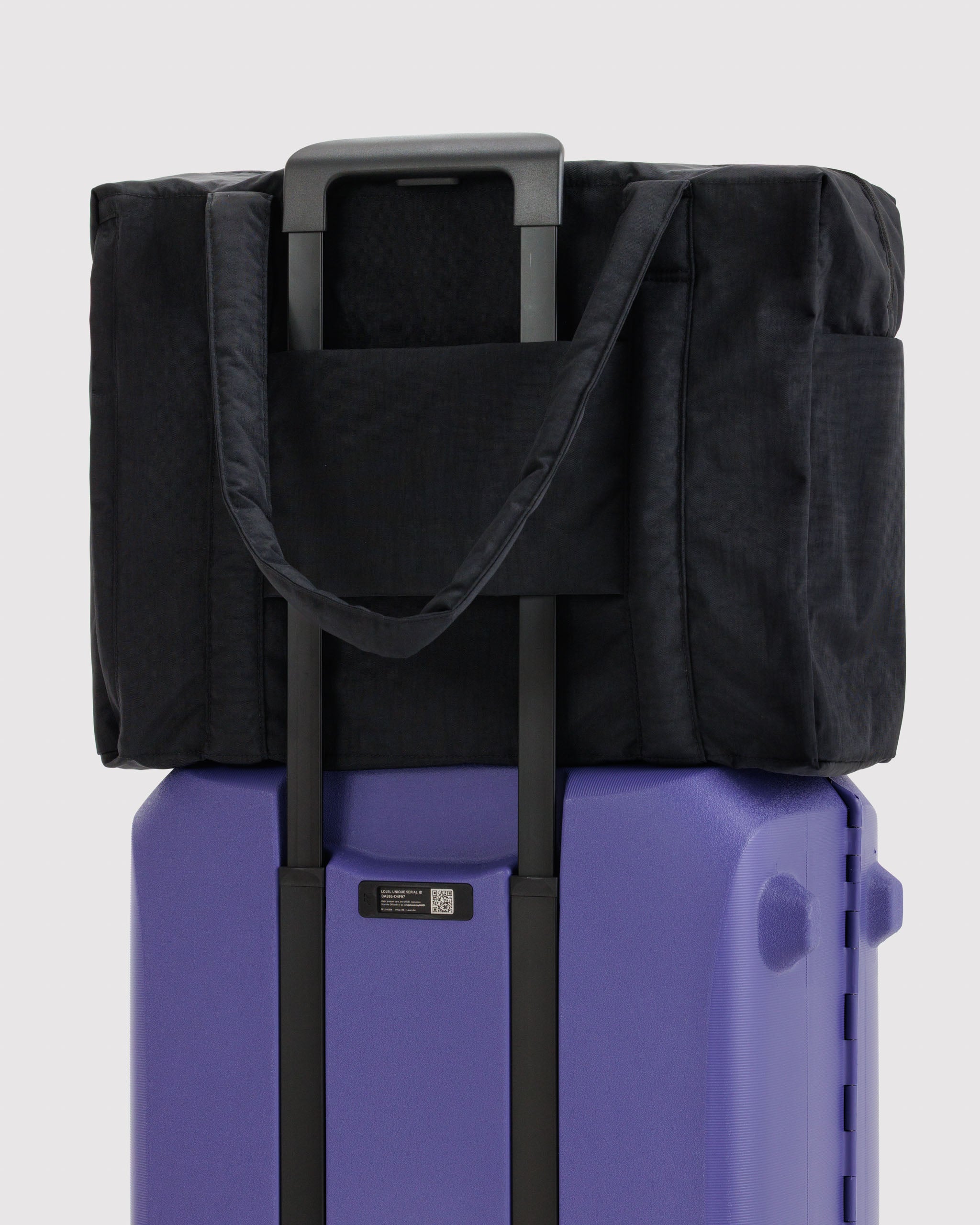 Black bag with trolley sleeve attached to handles on a purple suitcase.