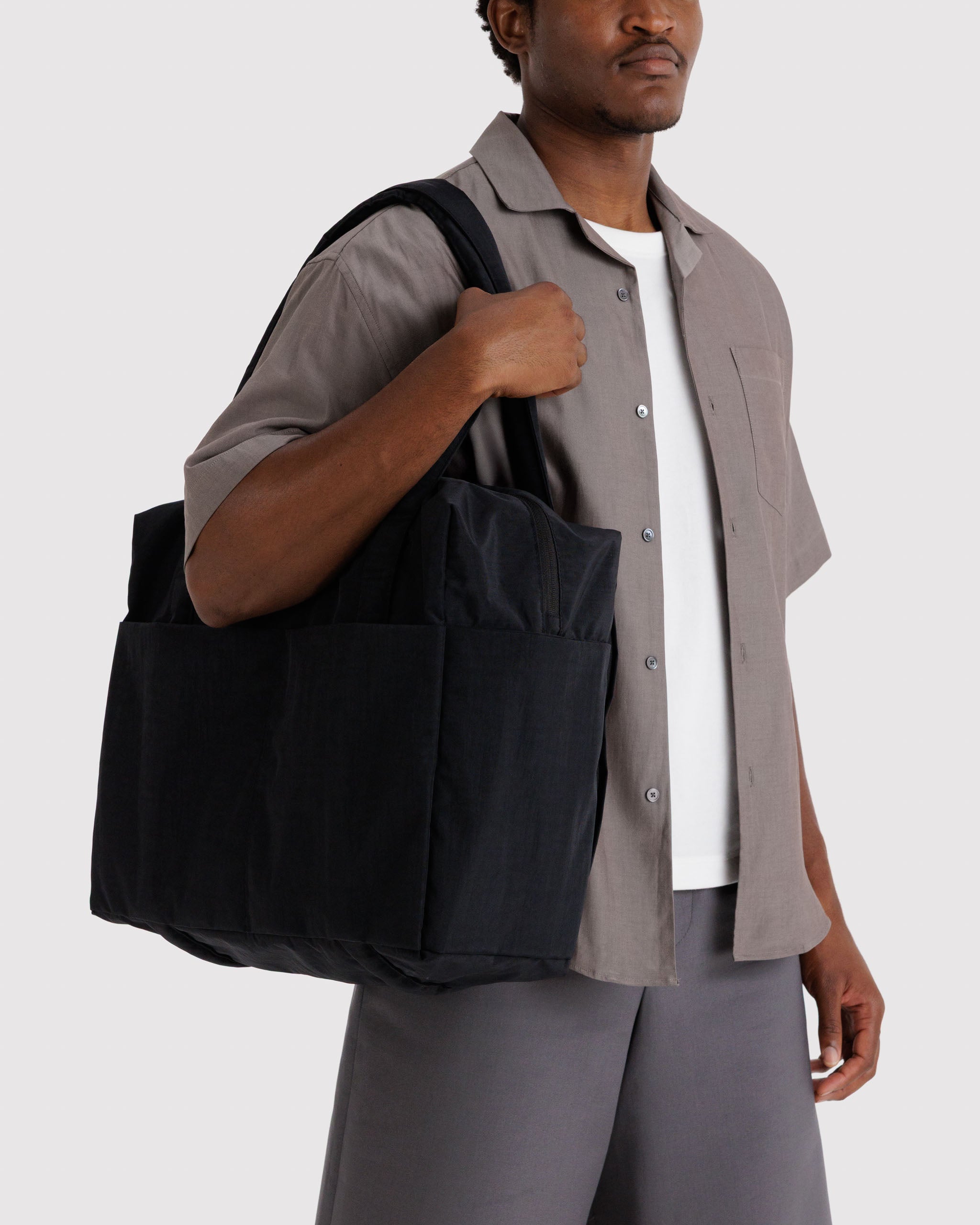 Man holding a black tote bag on shoulder.