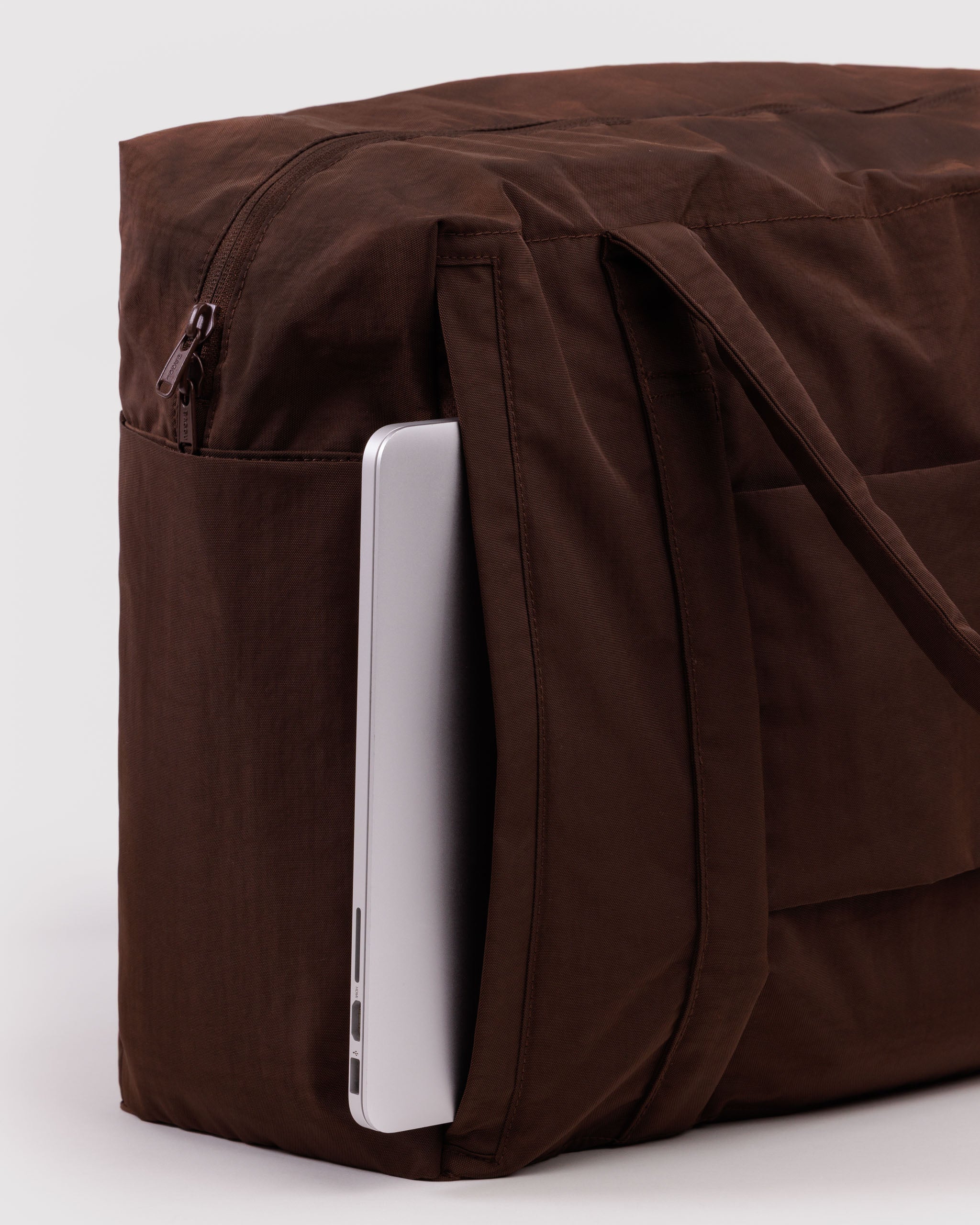 Brown tote bag with a laptop sticking out of a zip compartment at back of bag.