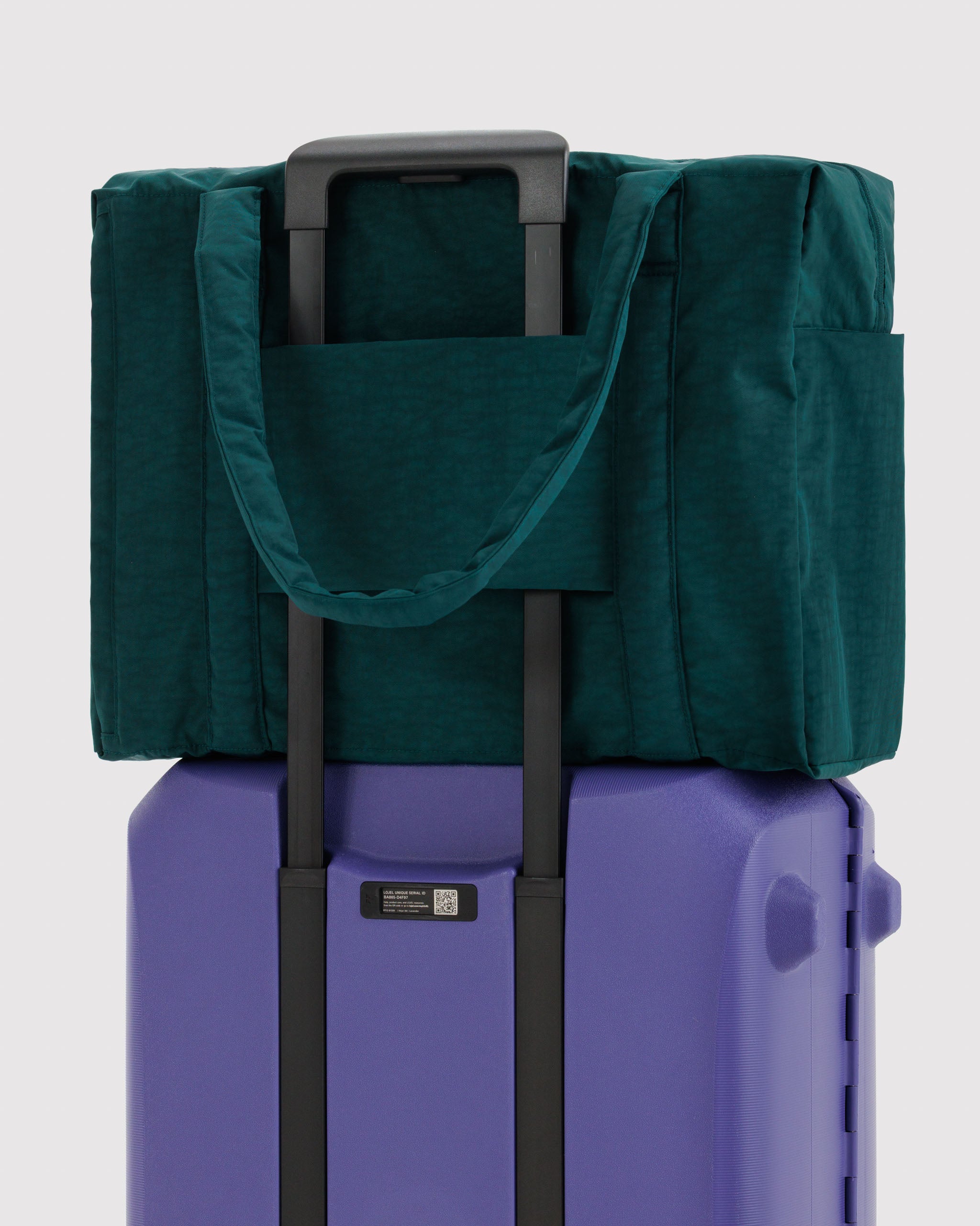 Green bag on top of a purple suitcase with trolley sleeve over handle.
