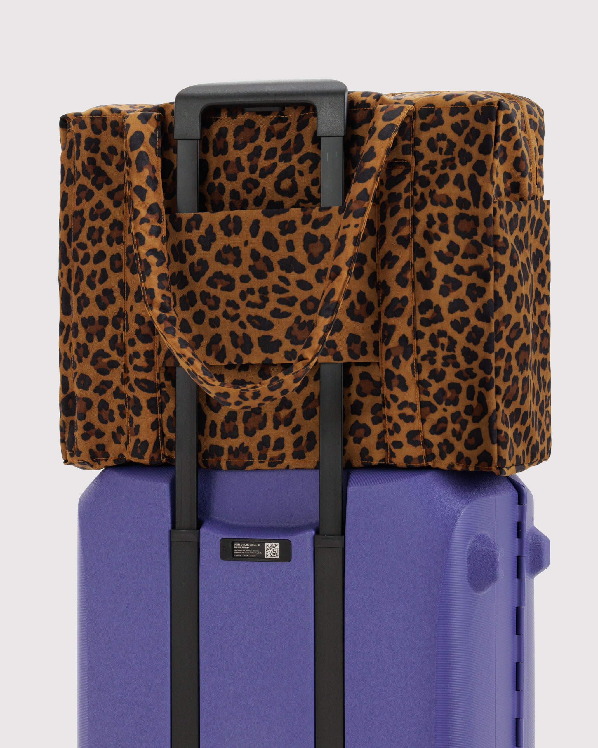 Purple suitcase with a leopard print duffle bag sitting on top attached by trolley sleeve.
