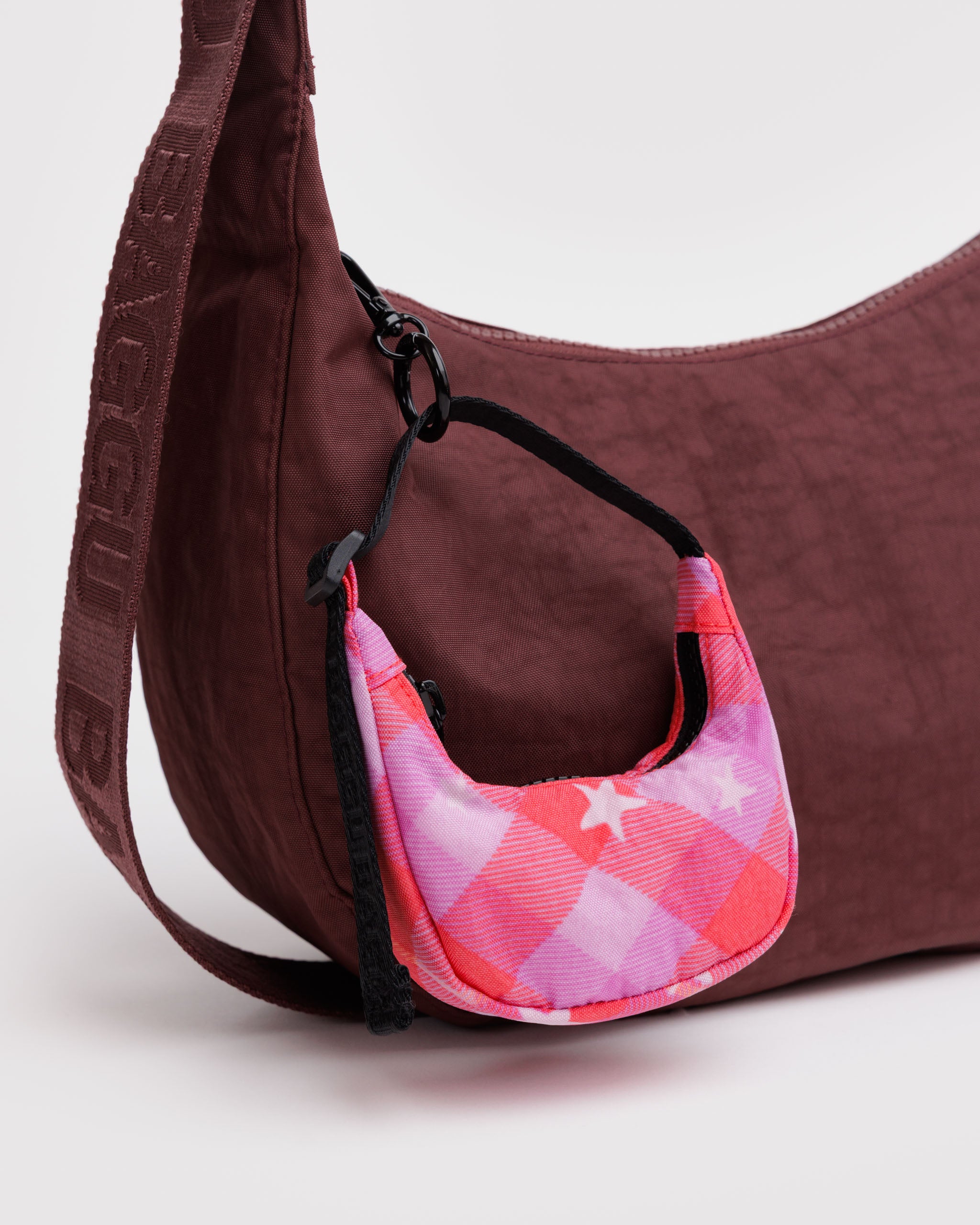 Burgundy handbag with a pink and red checkered pattern with stars print crescent bag charm attached by black keyring.