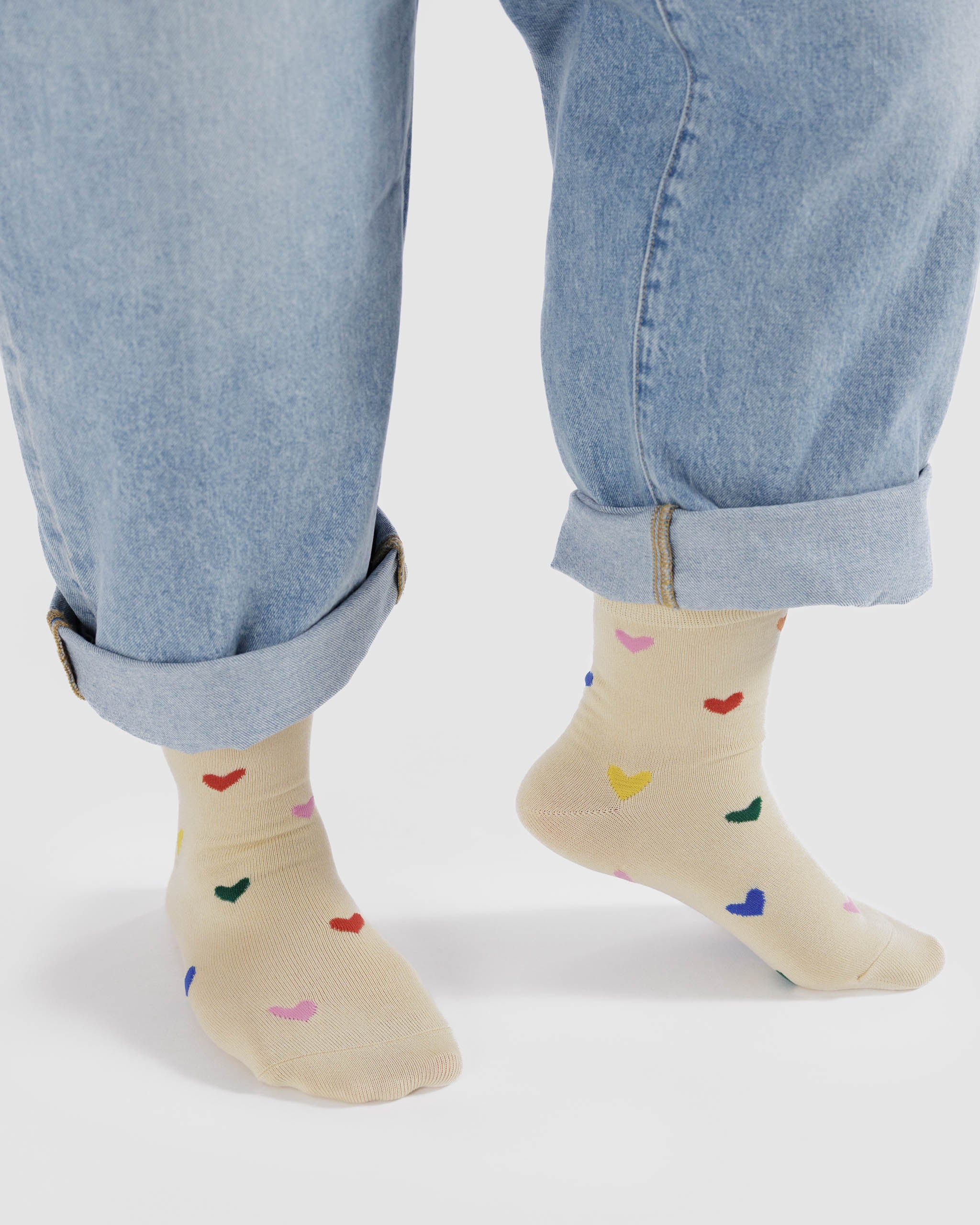 Person wearing cream socks with colourful heart patterns worn with rolled-up blue jeans.