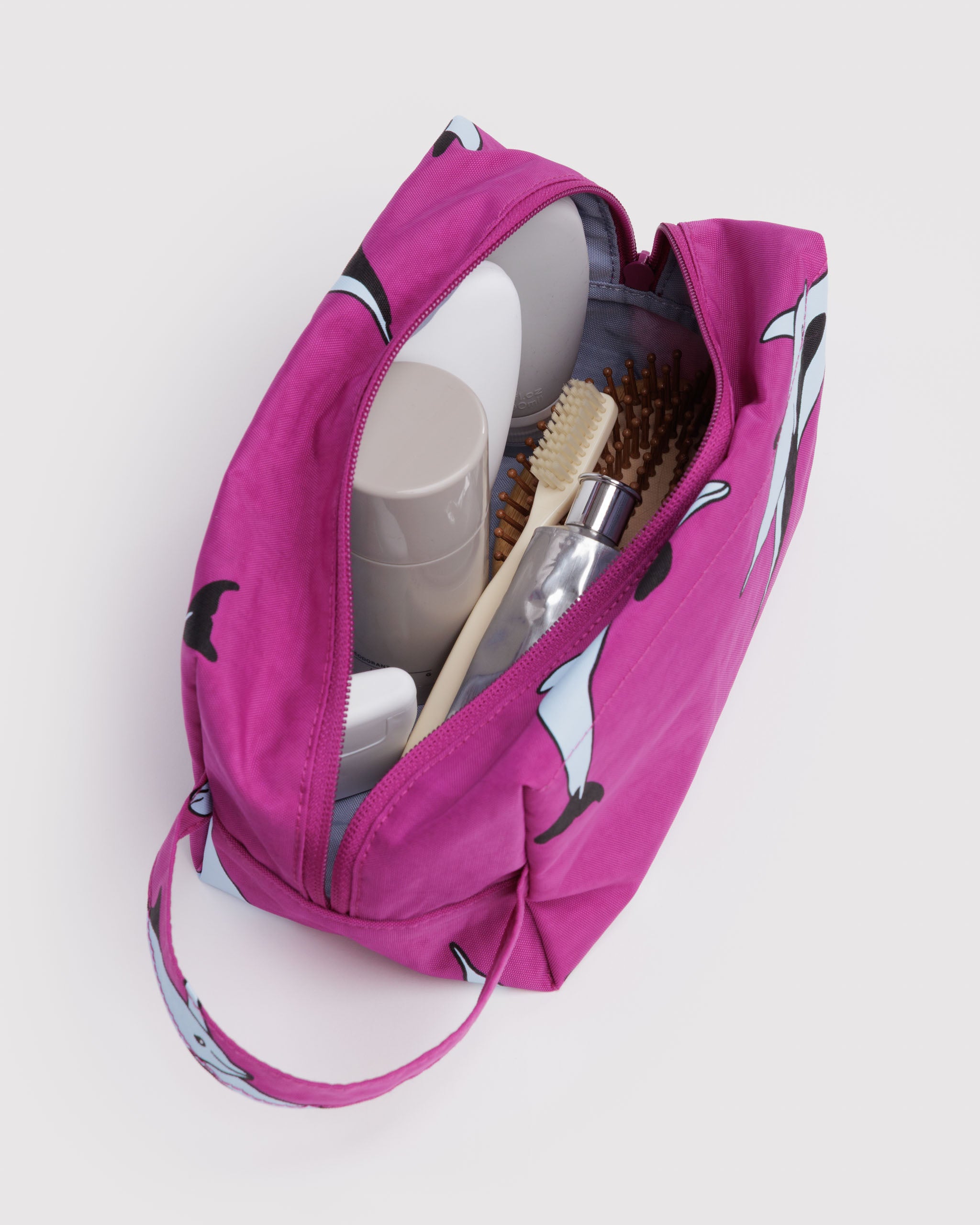Pink toiletry bag with dolphin patern and items inside and carry handle