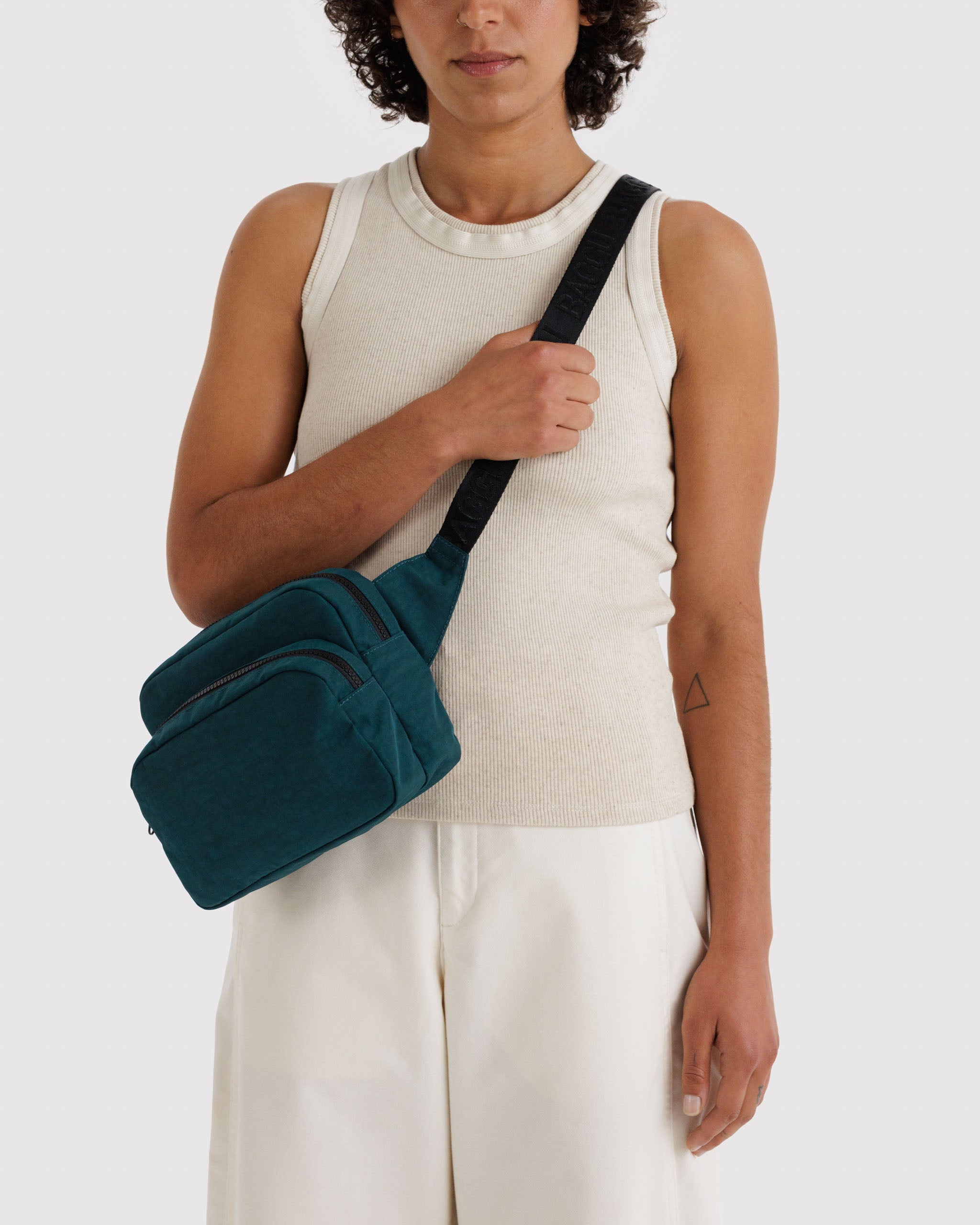 Person wearing a teal fanny pack crossbody holding the black webbed strap.