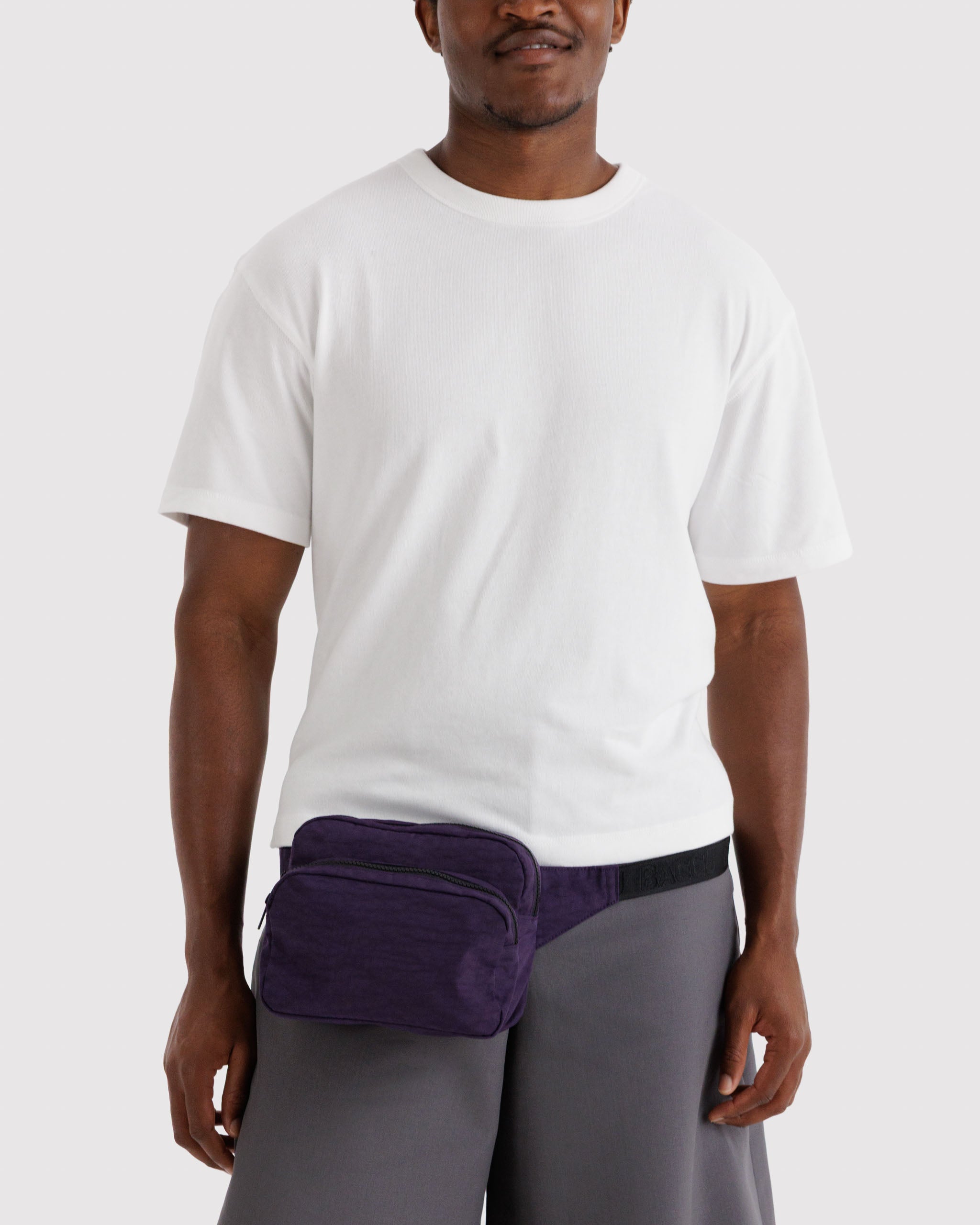 Man wearing a white t-shirt and grey pants with a purple fanny pack around waist.
