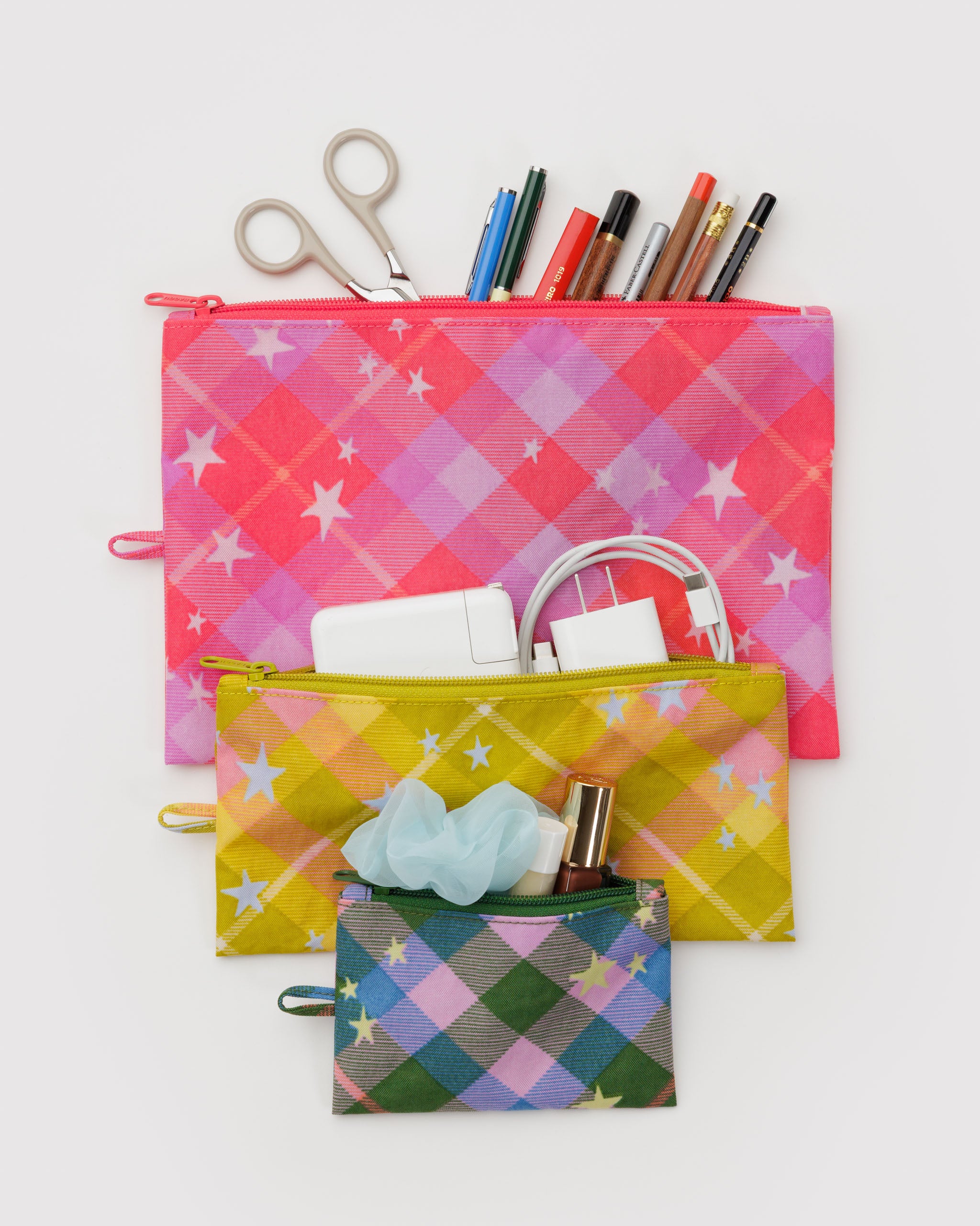 Three different sized colourful plaid pouches with stationery items, tech cords and makeup.