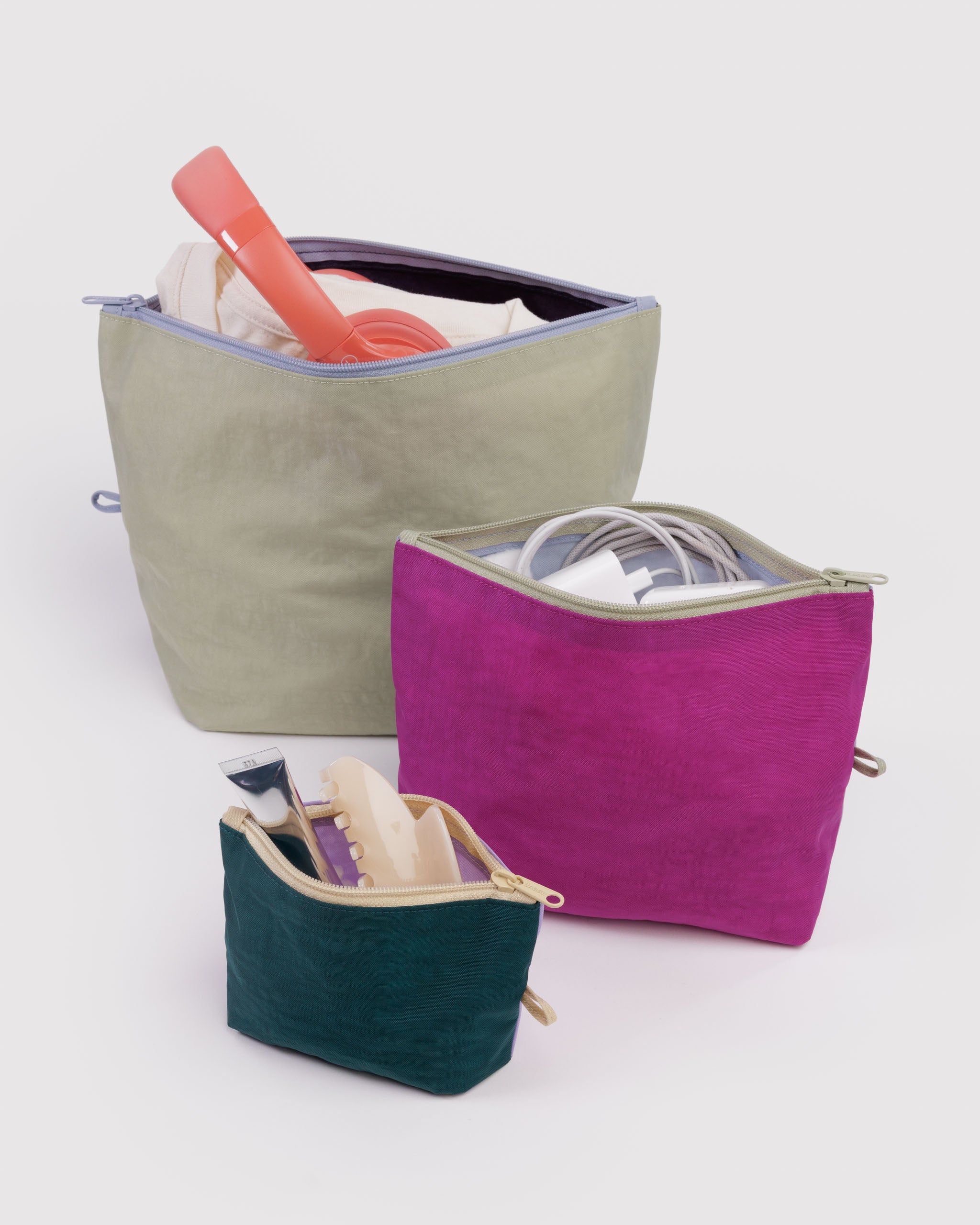 Three zip top bags in green, purple, and pink expanding with packed with items and standing flat on bottom.