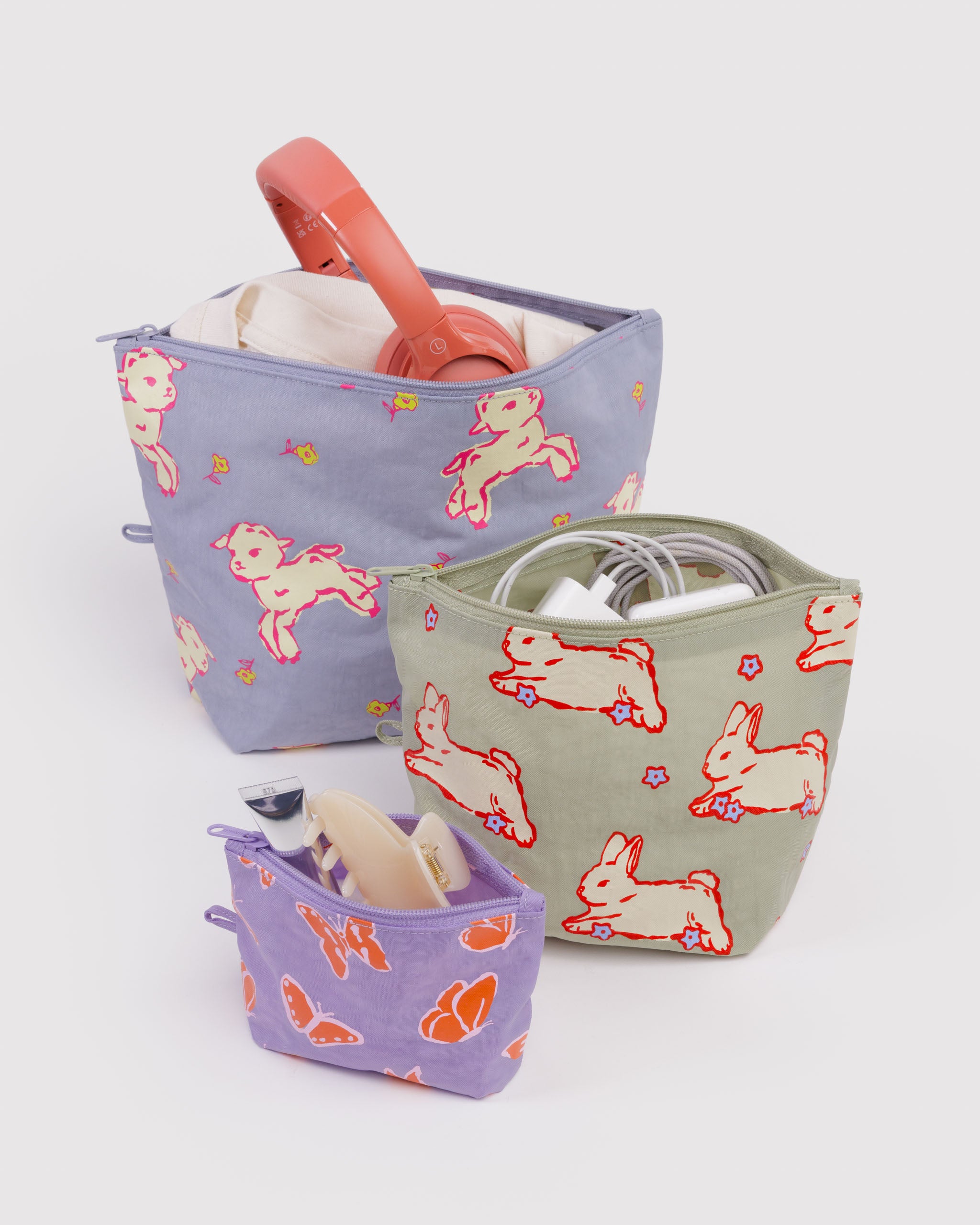 Set of three fabric bags with rabbit, bunny and butterfly patterns with zip top open and items packed inside standing on expandable flat bottom base.