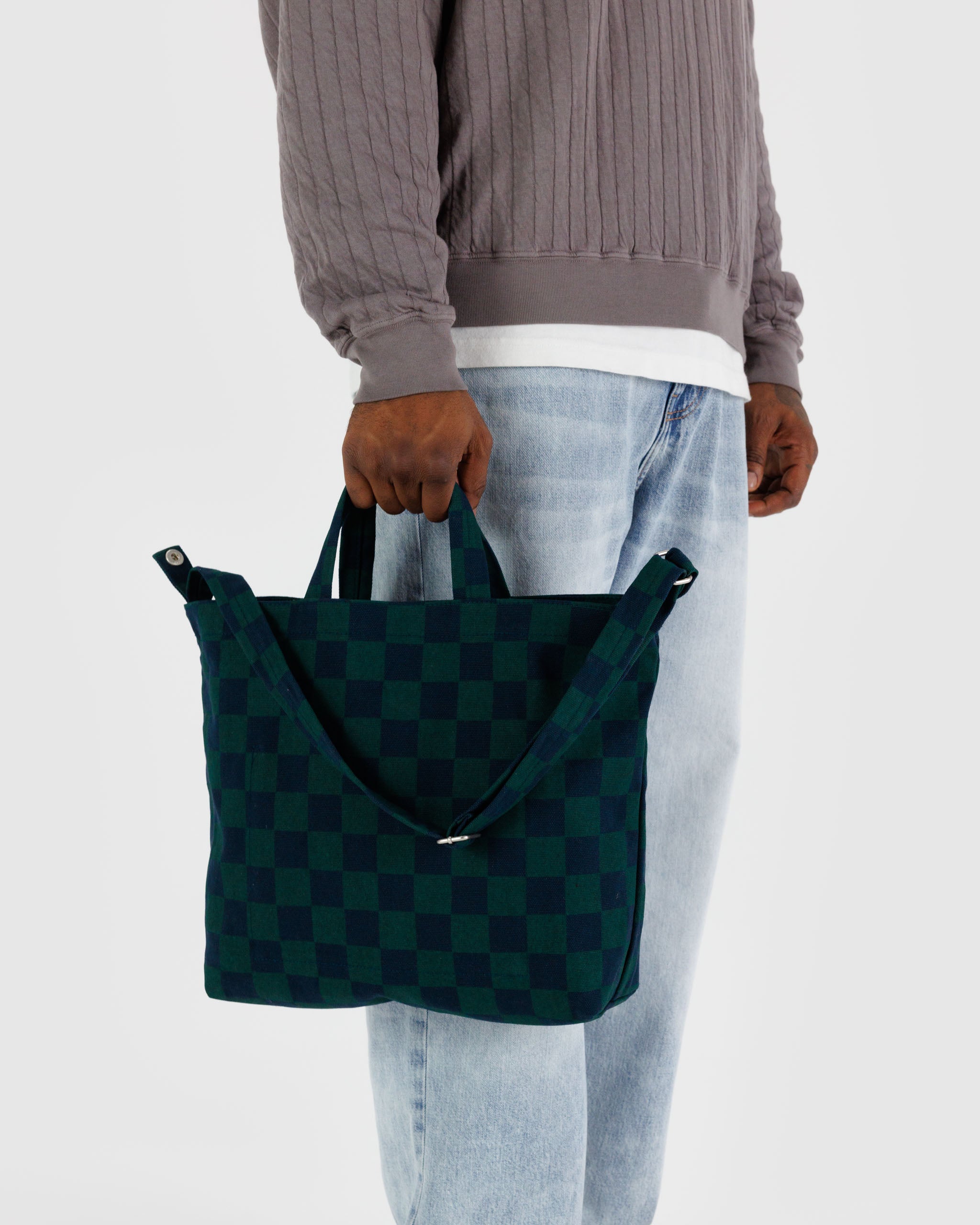 male-holding-short-carry-handles-of-wide-canvas-tote-navy-green-check-bag-with-long-adjustable-shoulder-strap