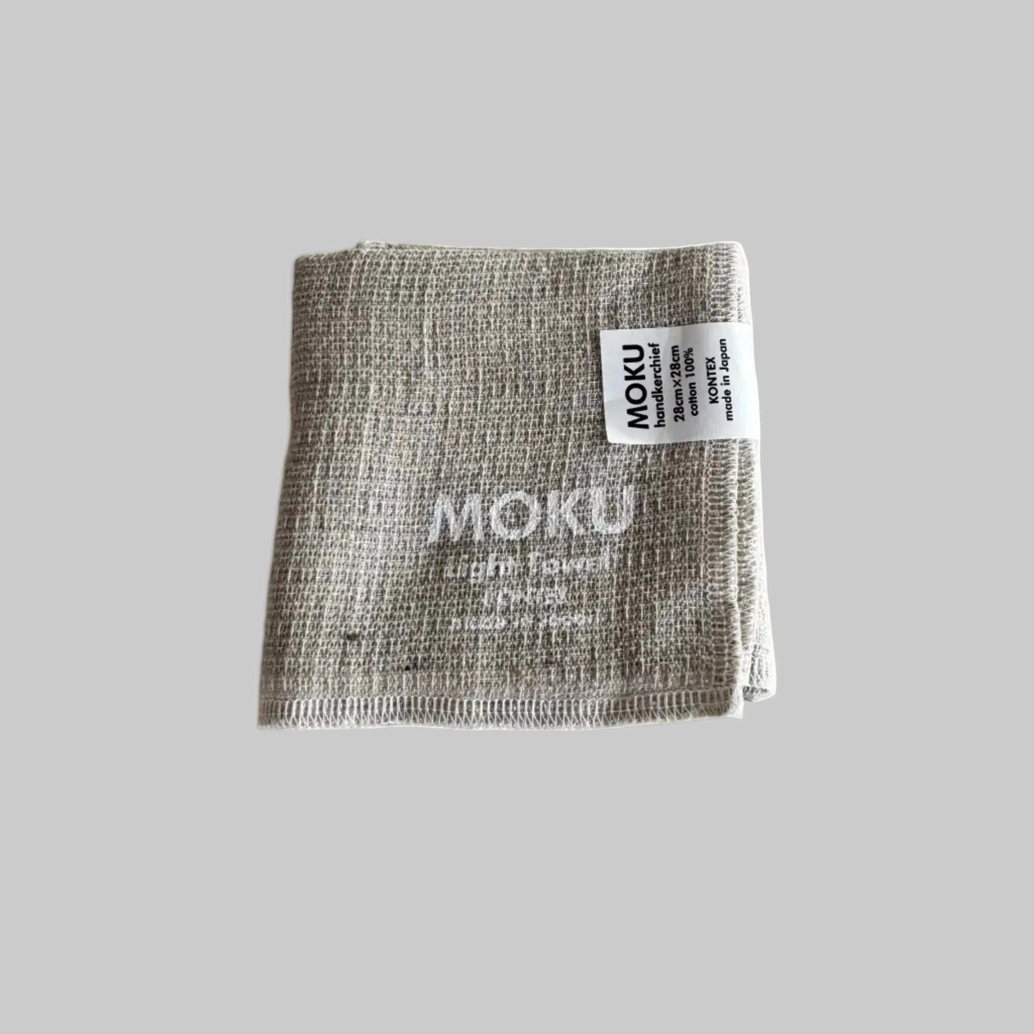 Folded natural face washer with 'MOKU Light Towel' written in white and a label.