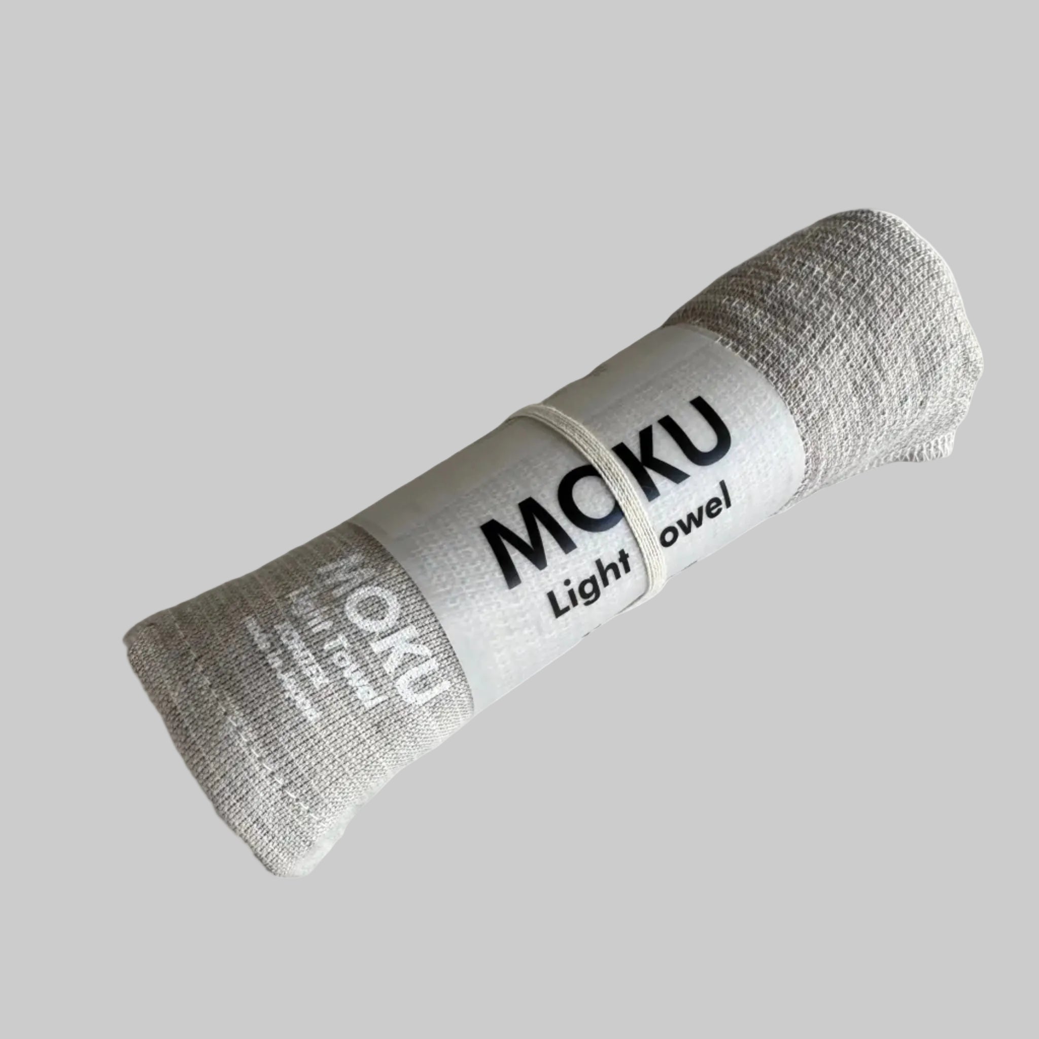 Natural coloured towel rolled in packaging sleeve with "MOKU Light Towel' written in white on fabric.