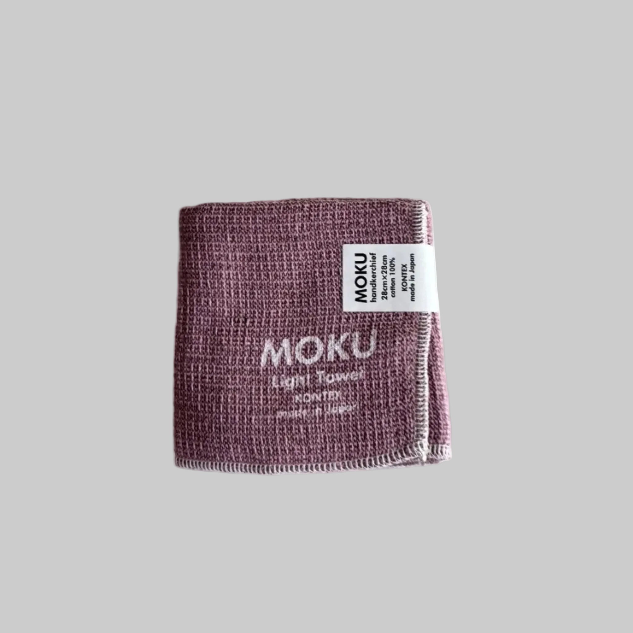 Folded pink face washer with 'MOKU Light Towel' written in white and a label.