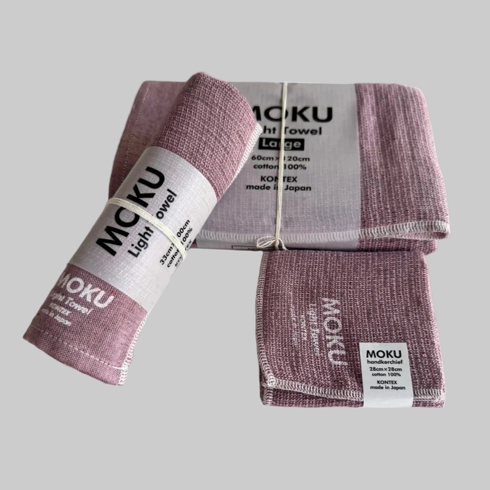 Moku light bath towel set in face washer, hand towel and bath towel in pink each folded with a packaging sleeves and with white writing on fabric.