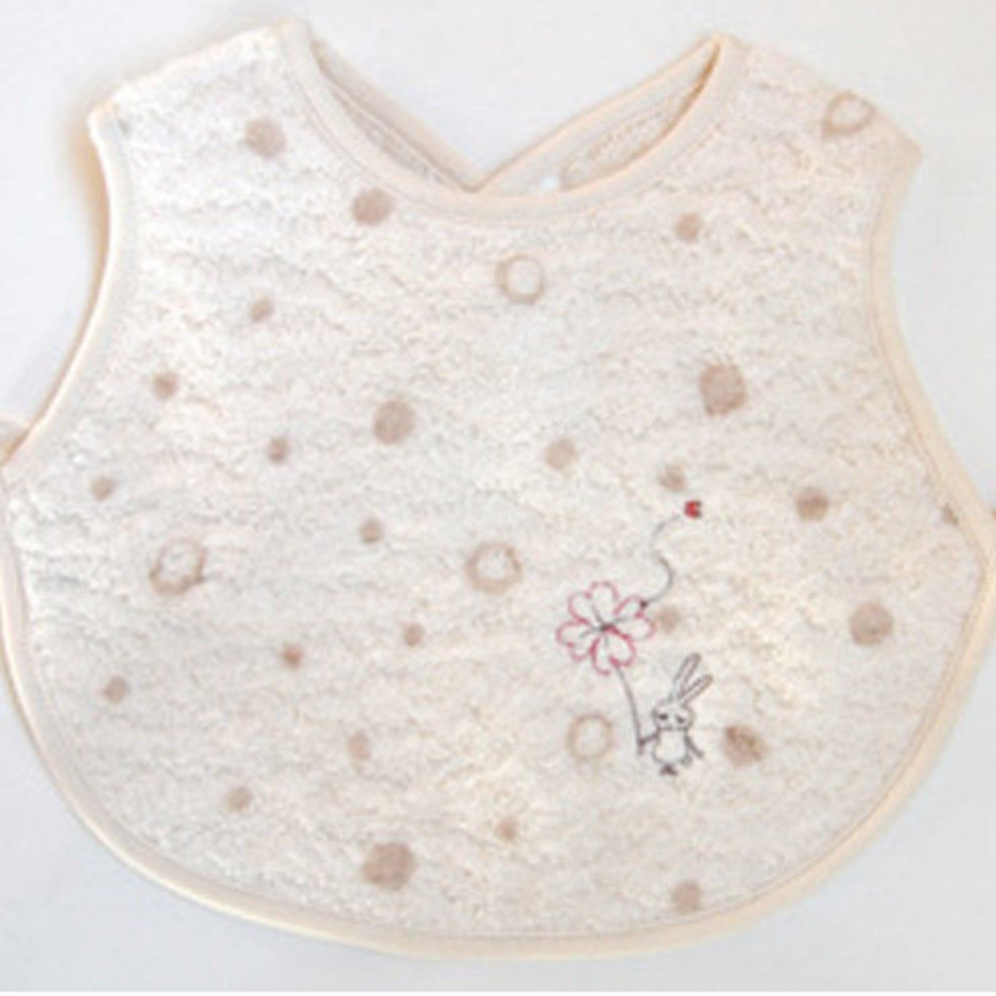 Cream baby apron bib with dots and embroidery design with back snap closure.