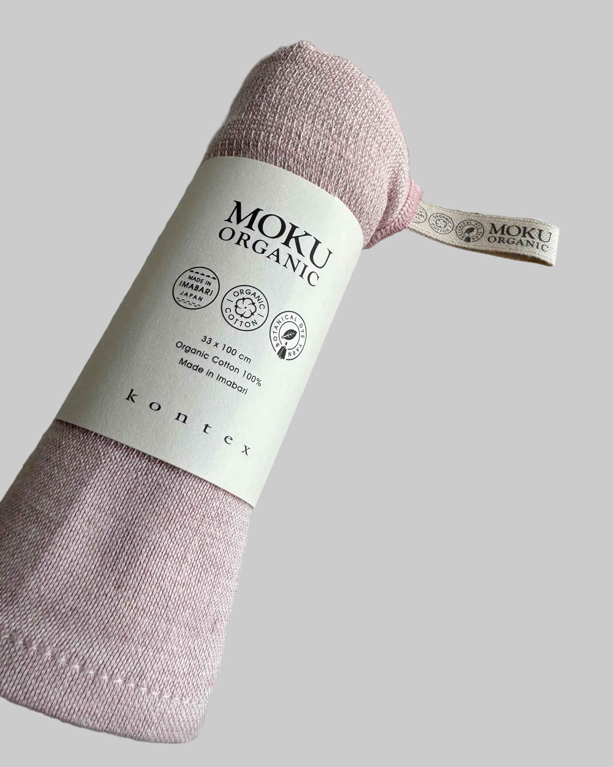 Pink organic cotton towel rolled in packaging sleeve with a 'MOKU Organic' label.