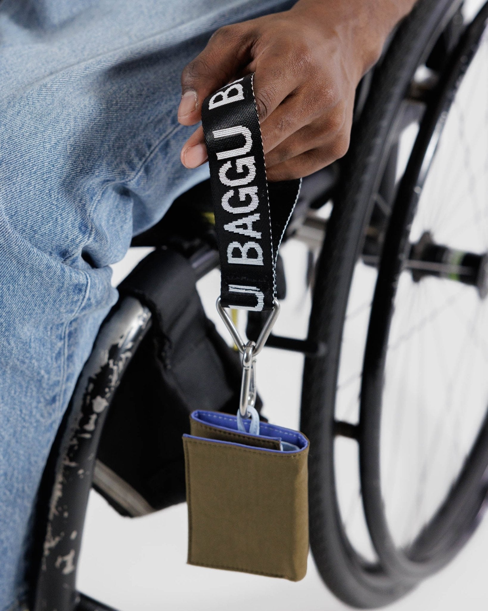 Man in a wheelchair holding a black and white Baggu Logo Keychain webbing strap with snap wallet attached - ANNIE.G
