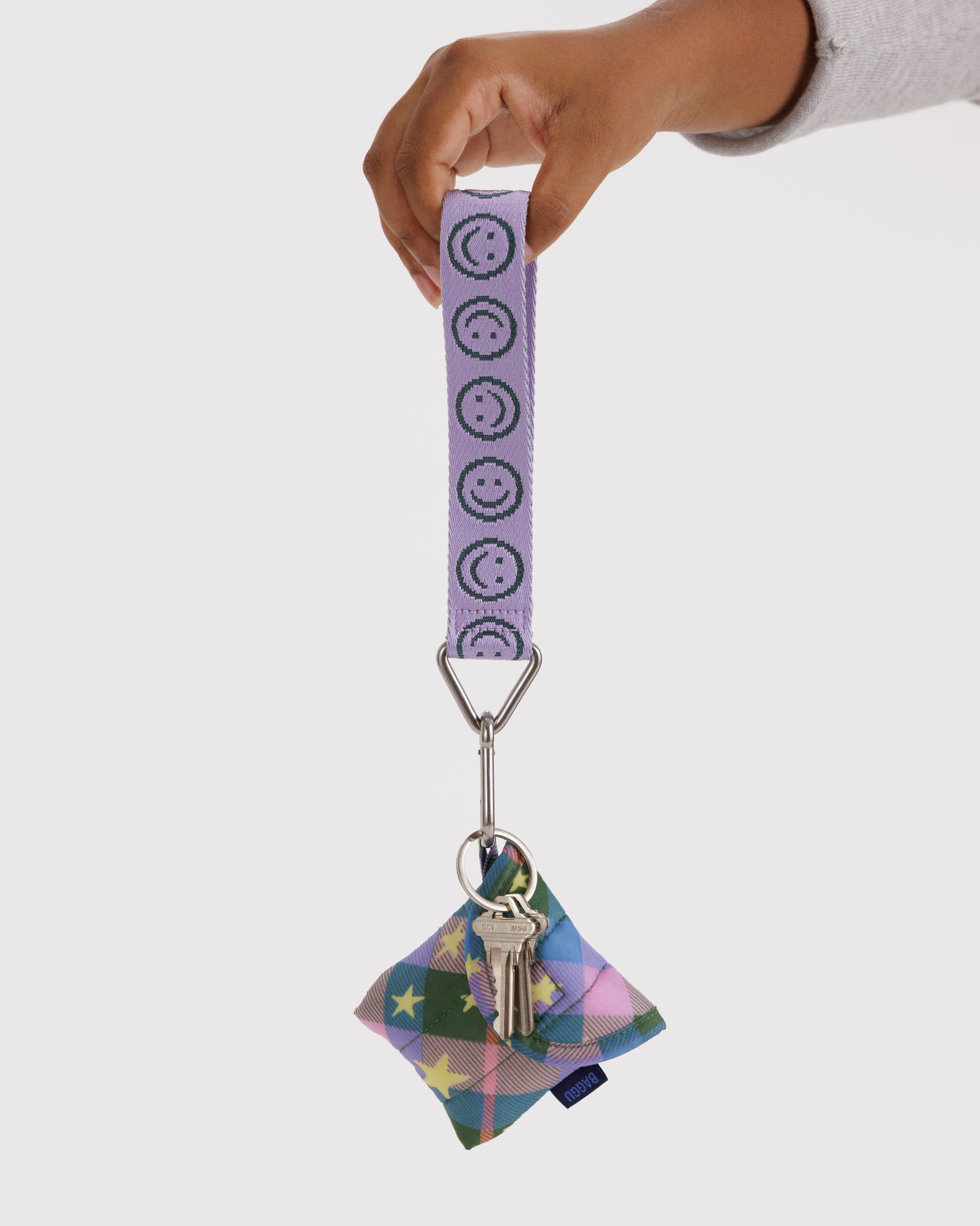 Lilac keychain with green smiley face patterned strap with earbuds case and keys attached held by a hand.