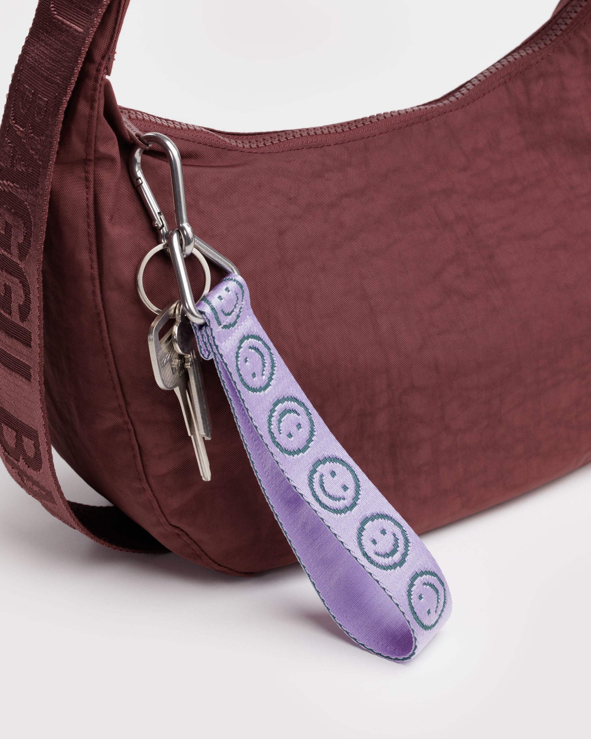 Maroon crescent bag with a lilac and green smiley face print key chain with keys attached to zip.