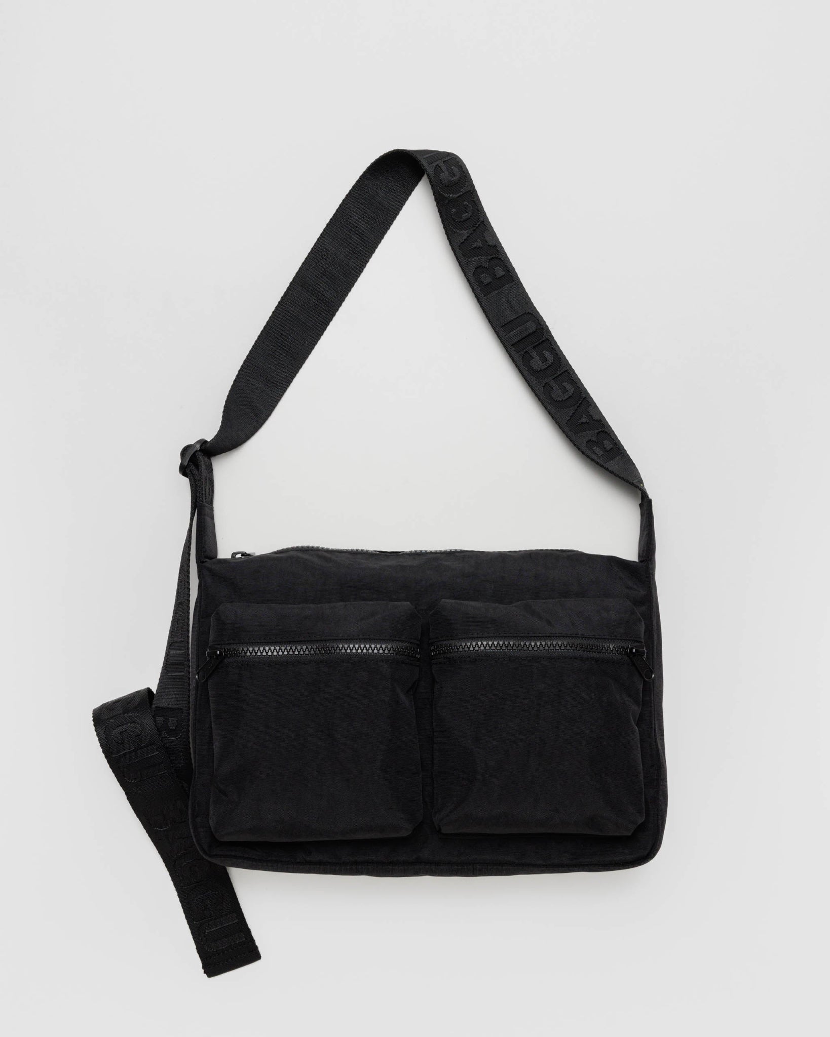 A black cargo crossbody bag with a wide webbed adjustable strap, zippered closures, and two front cargo pockets.
