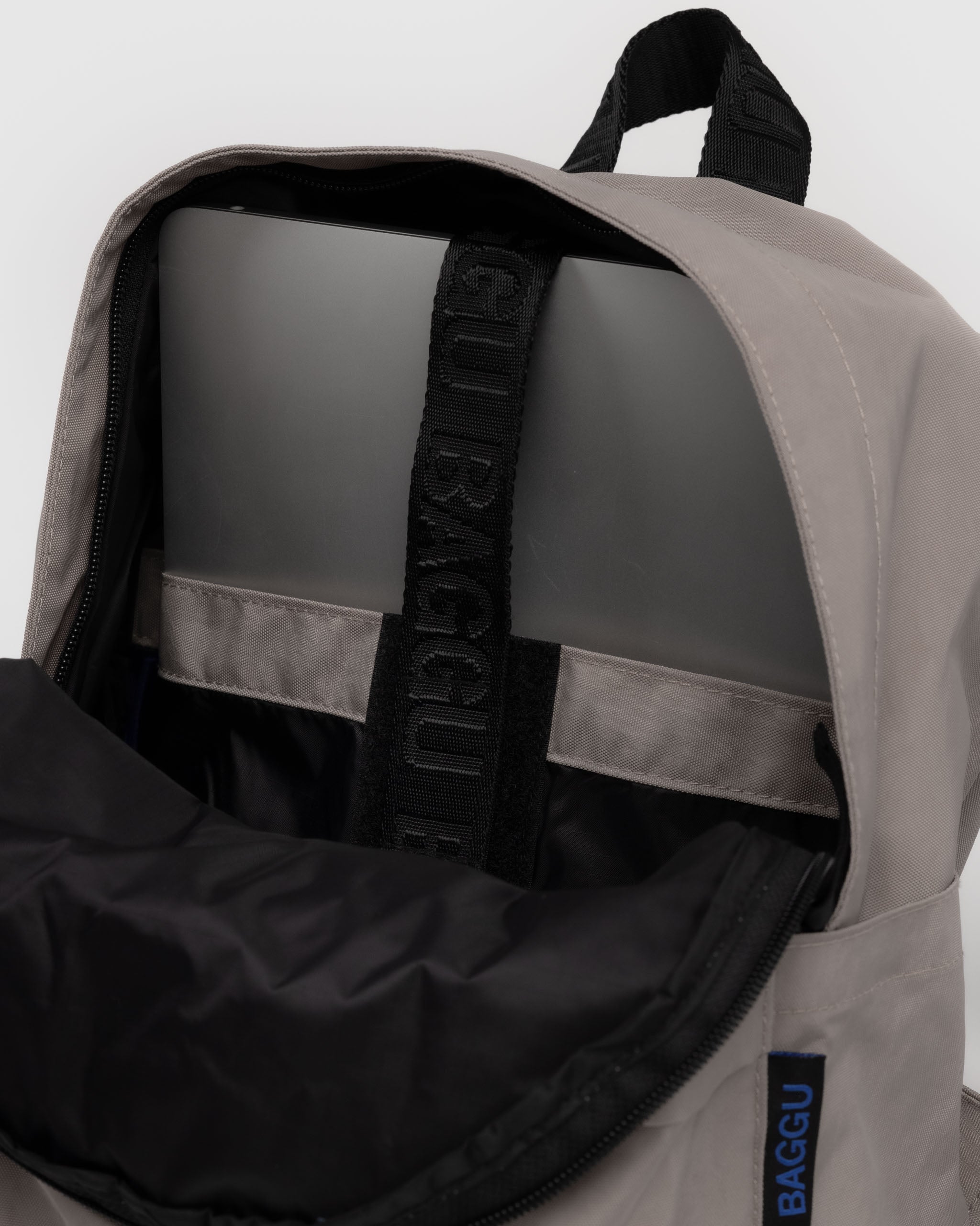 Light grey backpack with visible 'BAGGU' branding and inside laptop pocket, zip top and black carry handle at top