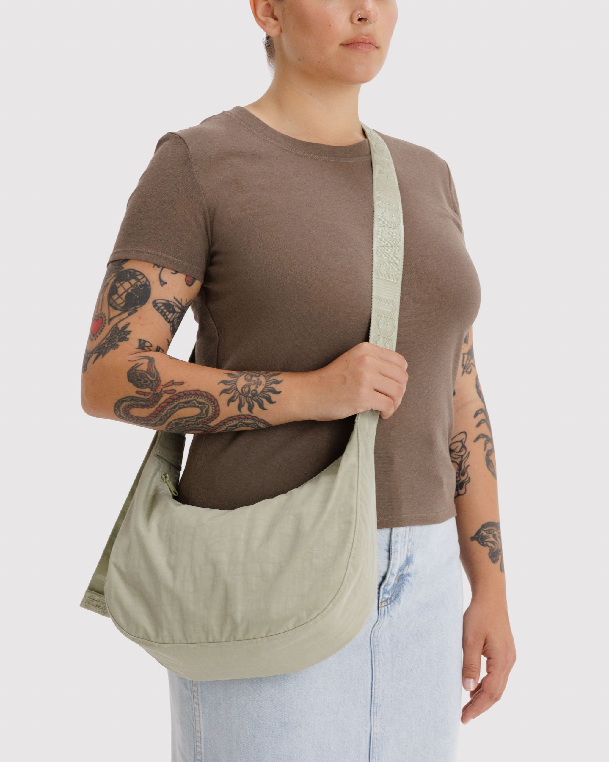 Person wearing a brown shirt and light blue jeans, holding a light green crossbody bag on shoulder.