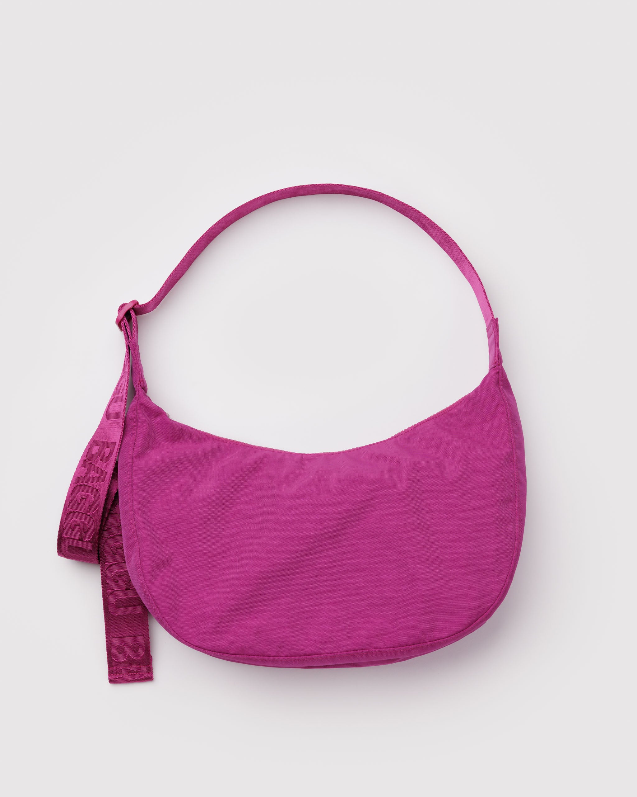 Vibrant pink crossbody bag in a crescent shape with a wide webbed adjustable strap and top zip.
