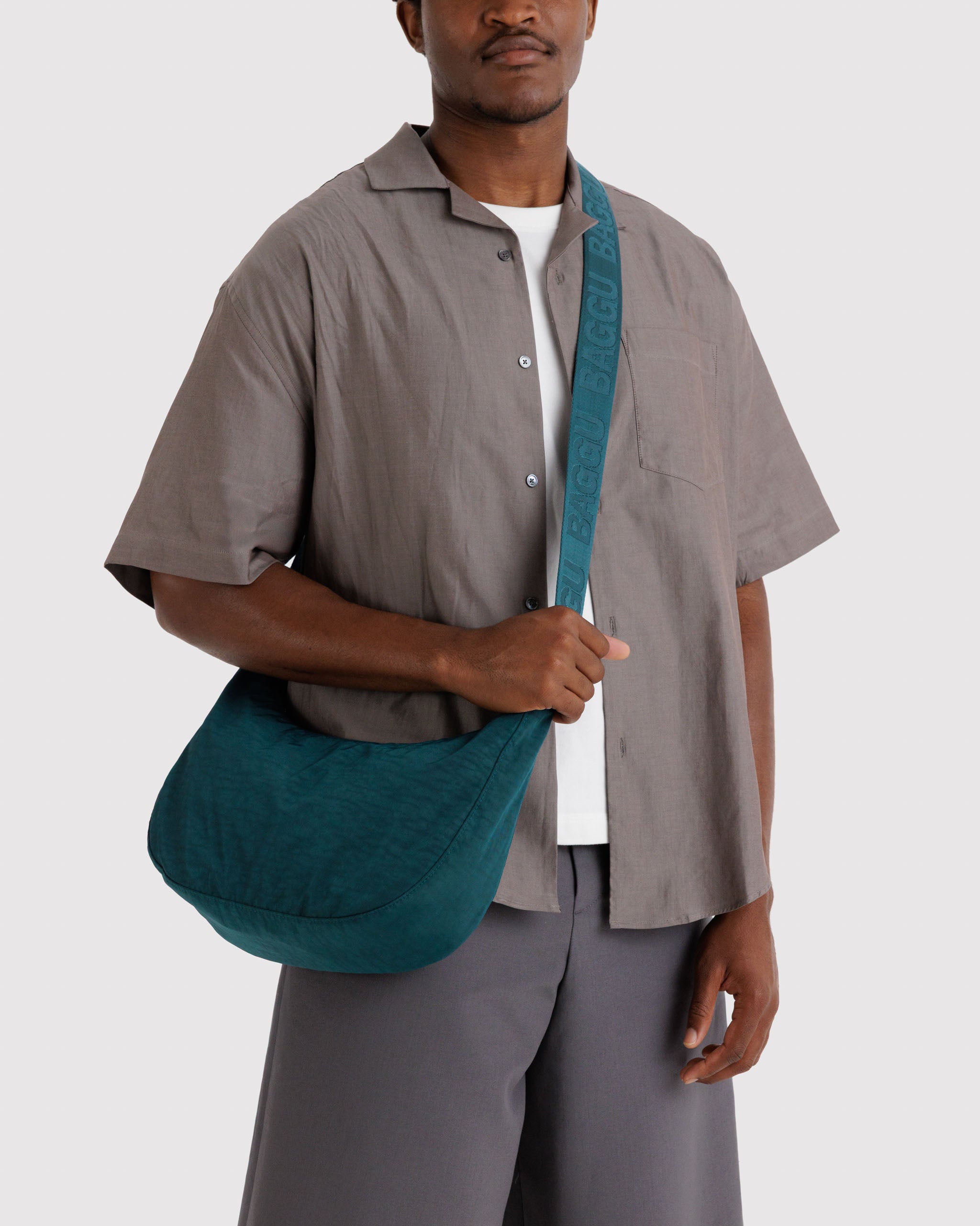 Man holding a teal bag crossbody on shoulder.